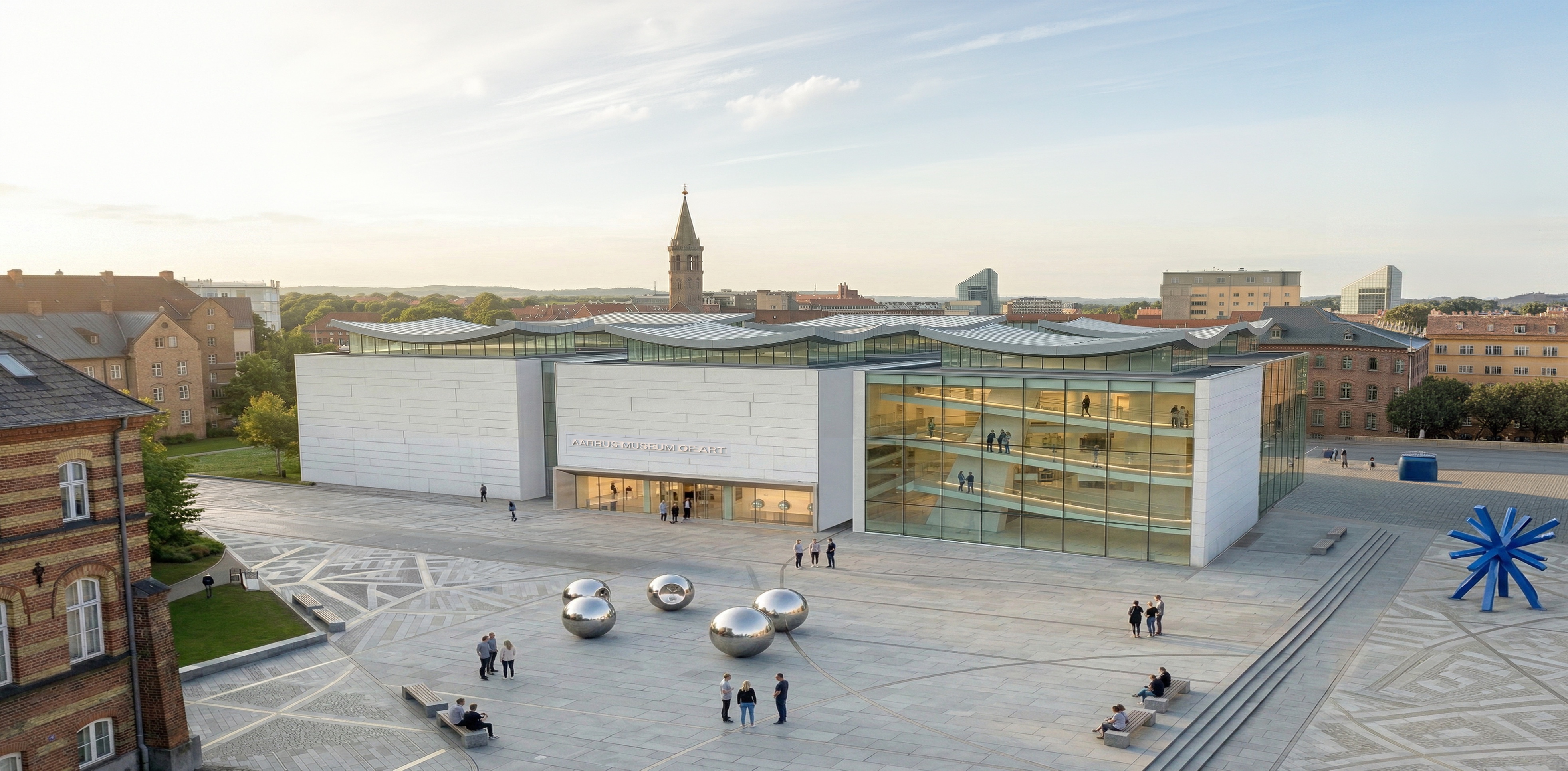 Aerial view of the Aarhus Museum of Contemporary Art with its white stone facade, undulating roofline, and reflective spheres on the public plaza