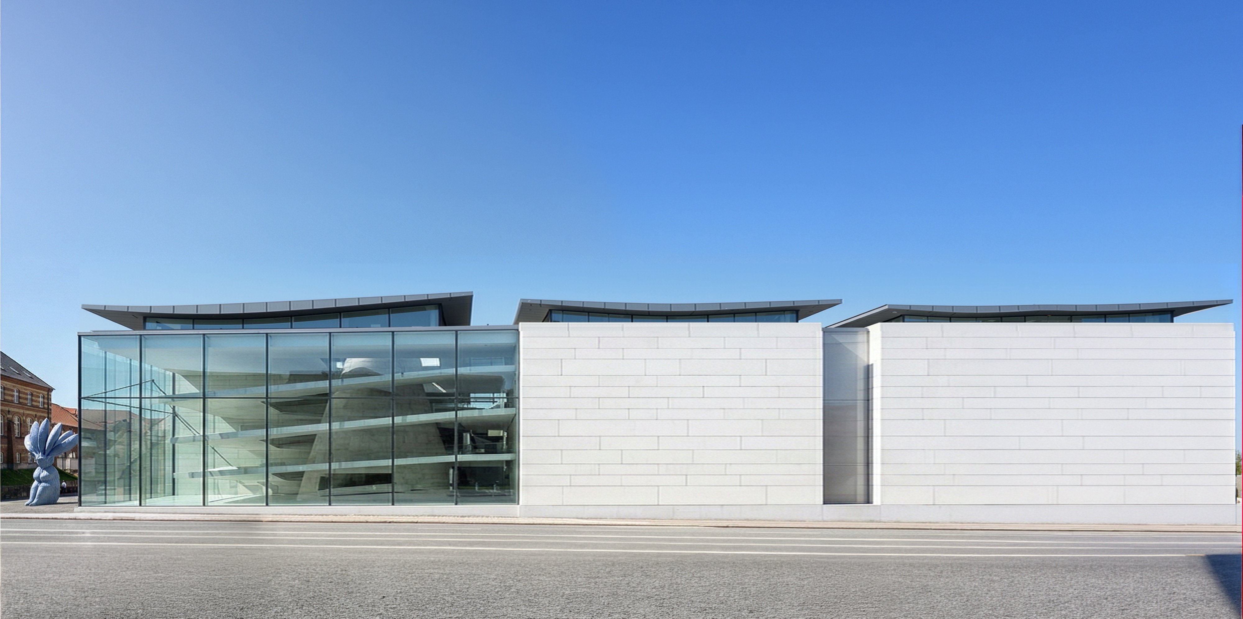 Street elevation of the museum showing the full-height glazed gallery wing and pale stone cladding under a clear sky