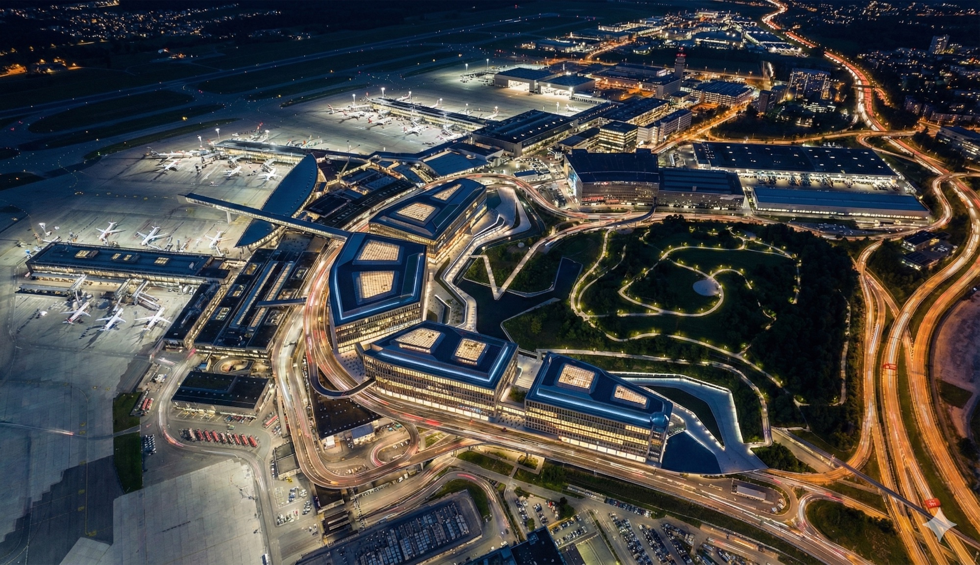 Wide night aerial showing The Circle's illuminated courtyards integrated within the full Zurich Airport campus