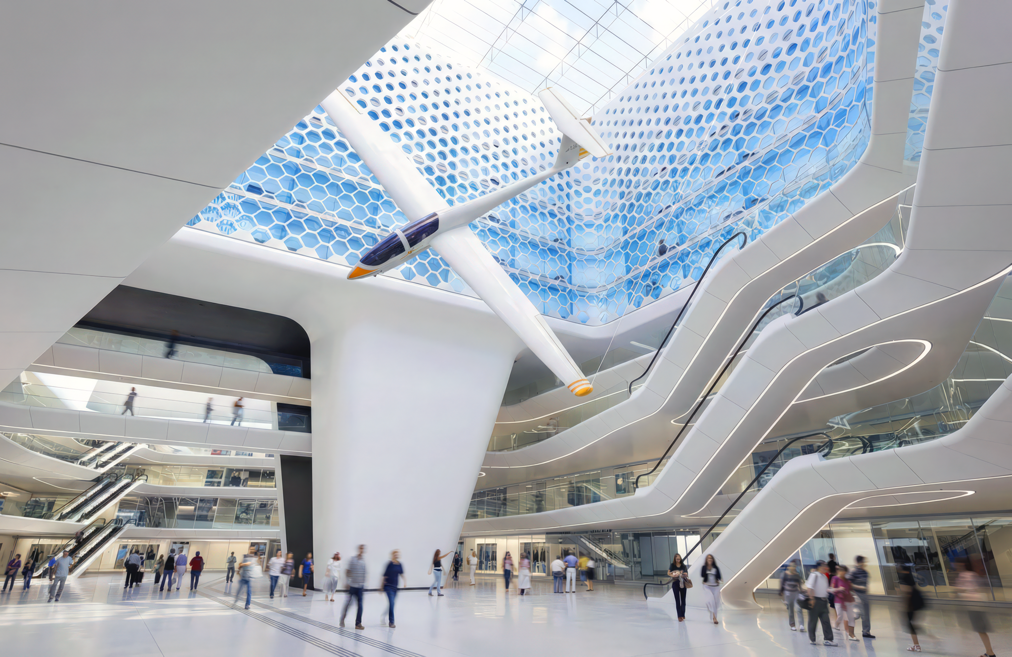 Multi-level interior atrium with flowing escalator ribbons and hexagonal glass skylight