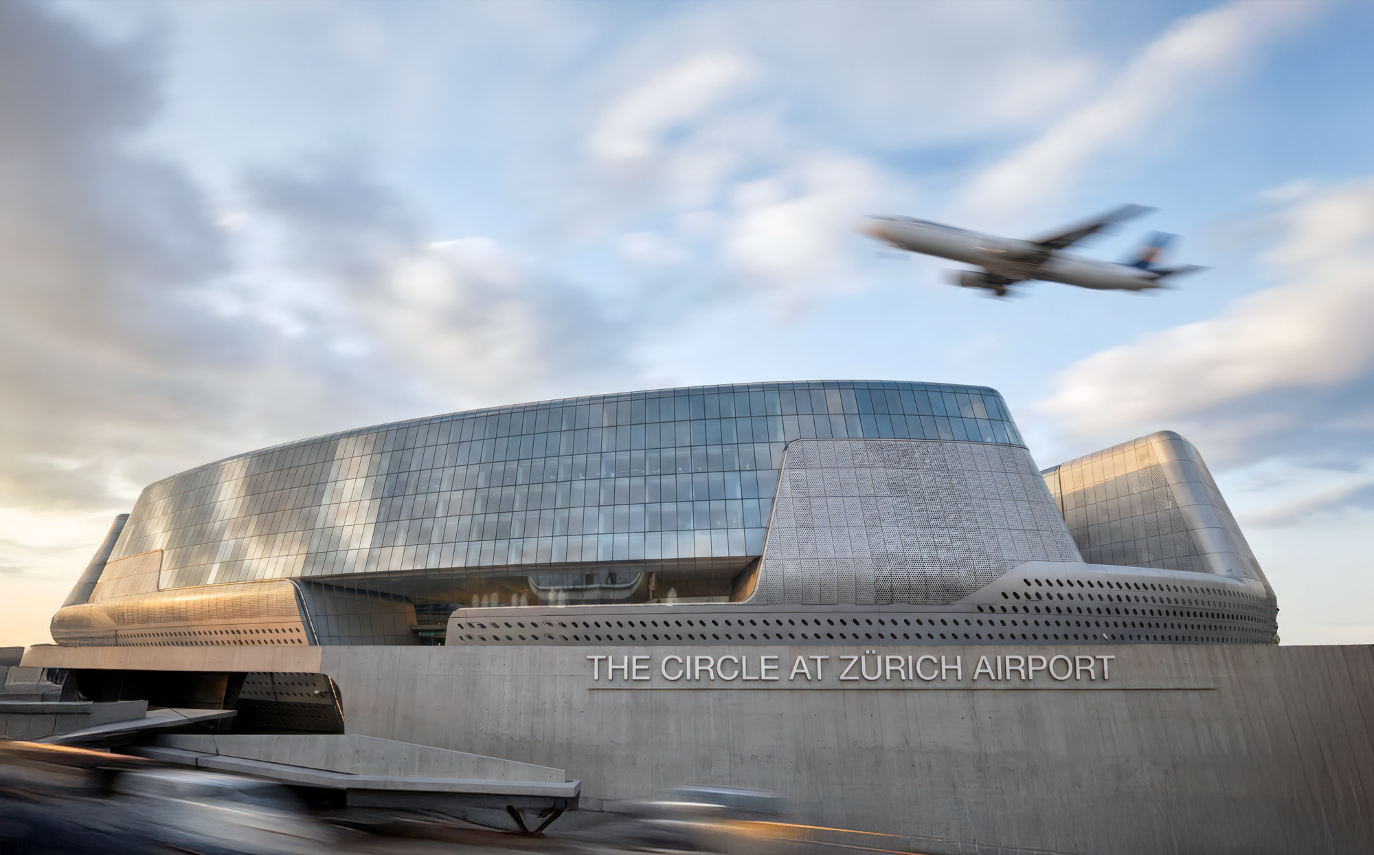 Exterior view with aircraft passing overhead, showing the building's metallic skin and honeycomb facade