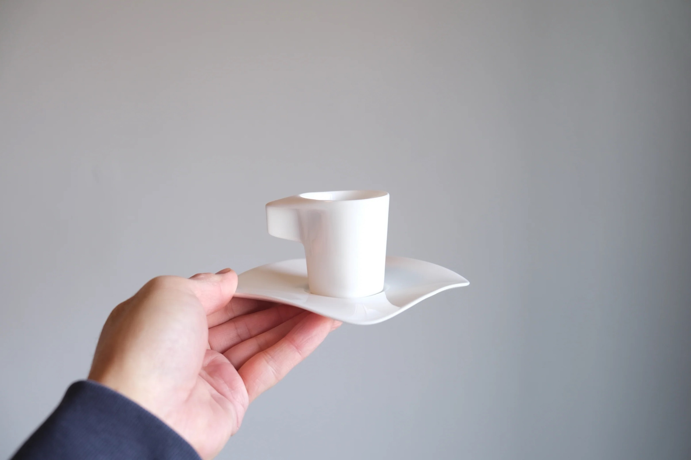 A hand holding a single Alessi espresso cup on its wave-form saucer