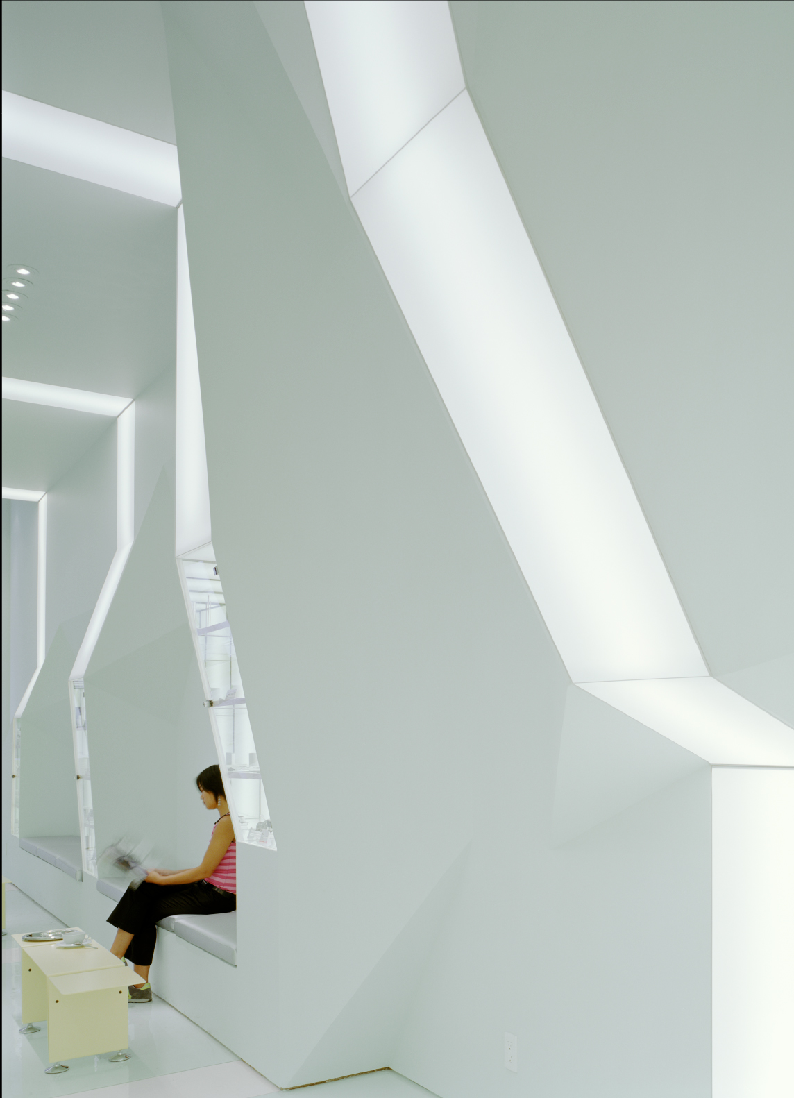 Detail of geometric ceiling manipulation and illuminated light band with visitor seated below