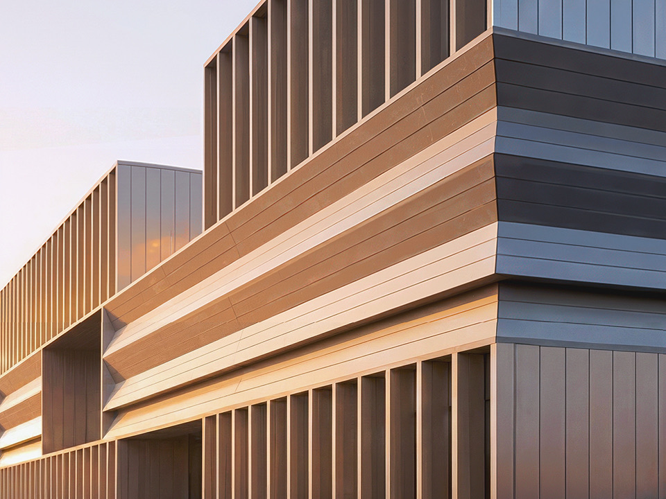 Close-up detail of the terminal facade showing stacked horizontal metal panels in warm bronze and cool grey tones at dusk