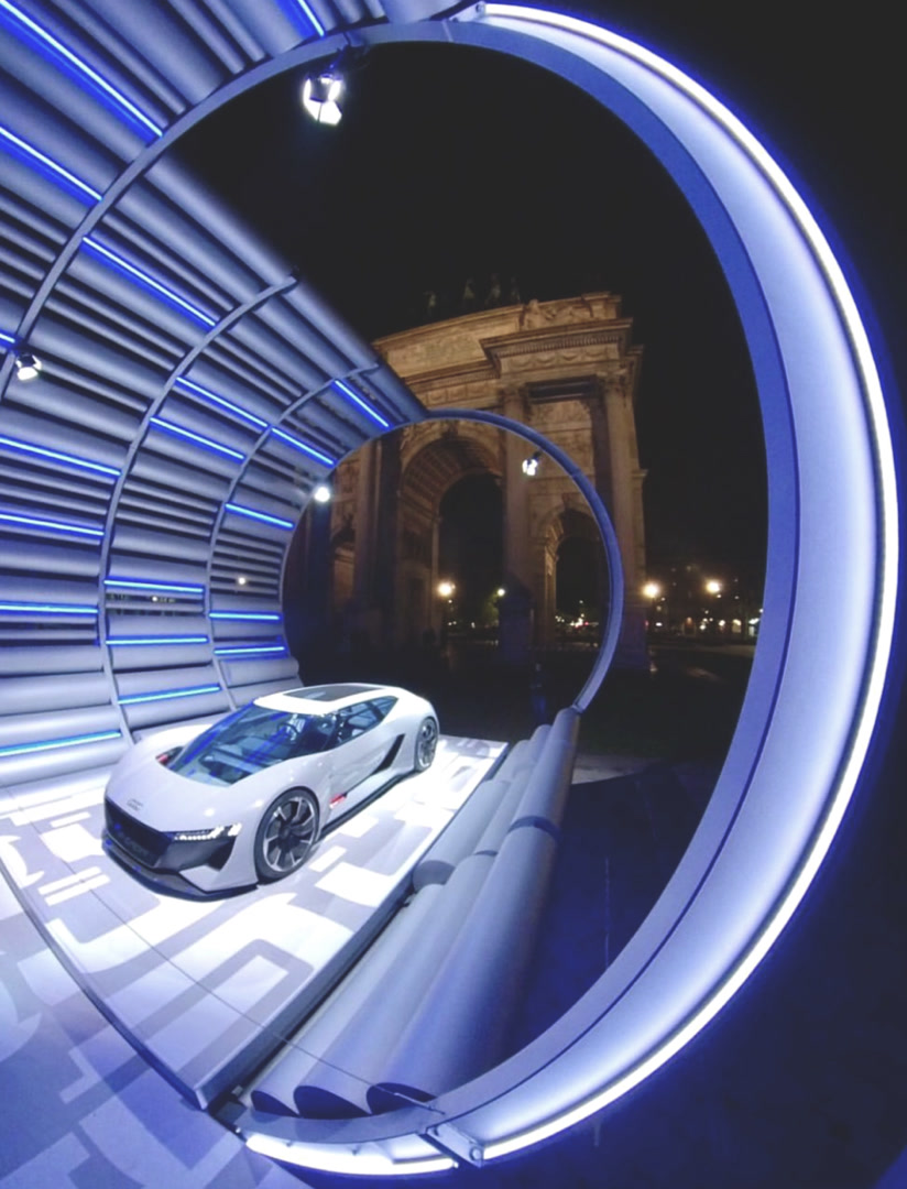 Side angle view of the E_Station with E-Tron vehicle framed by the illuminated ring and Arco della Pace beyond