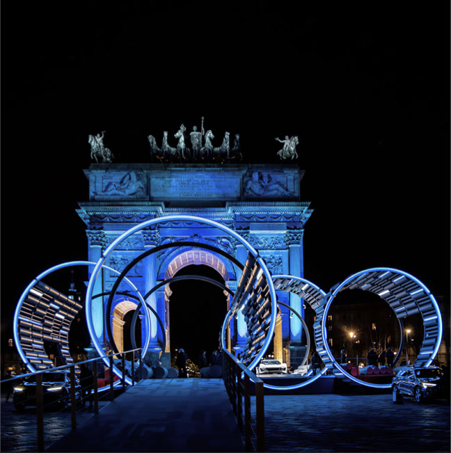 Night view of the full E_Station installation with illuminated rings in front of the Arco della Pace
