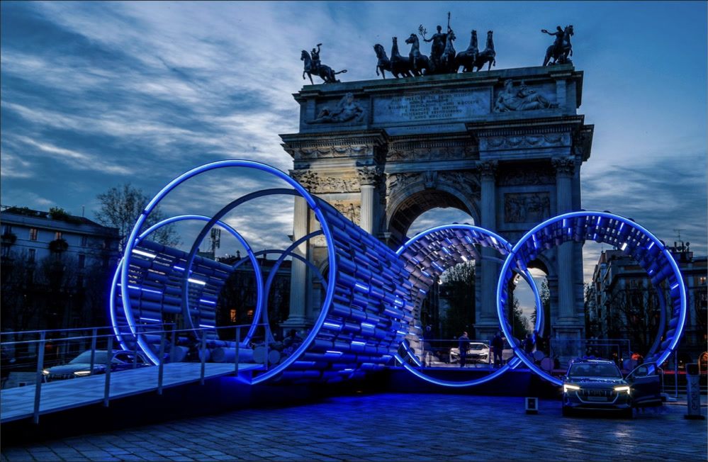 Dusk panoramic view of the E_Station pavilion with blue LED rings and the Arco della Pace