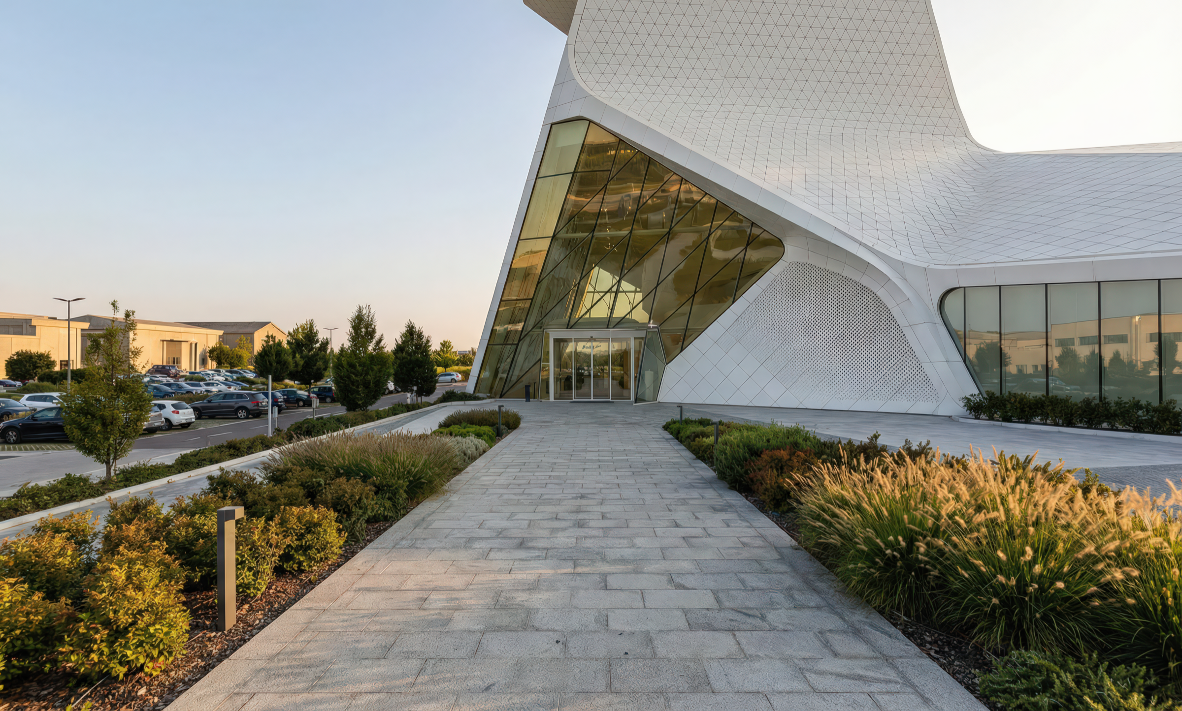 Landscaped stone pathway leading to the main entrance with triangulated glass curtain wall and white perforated cladding panels