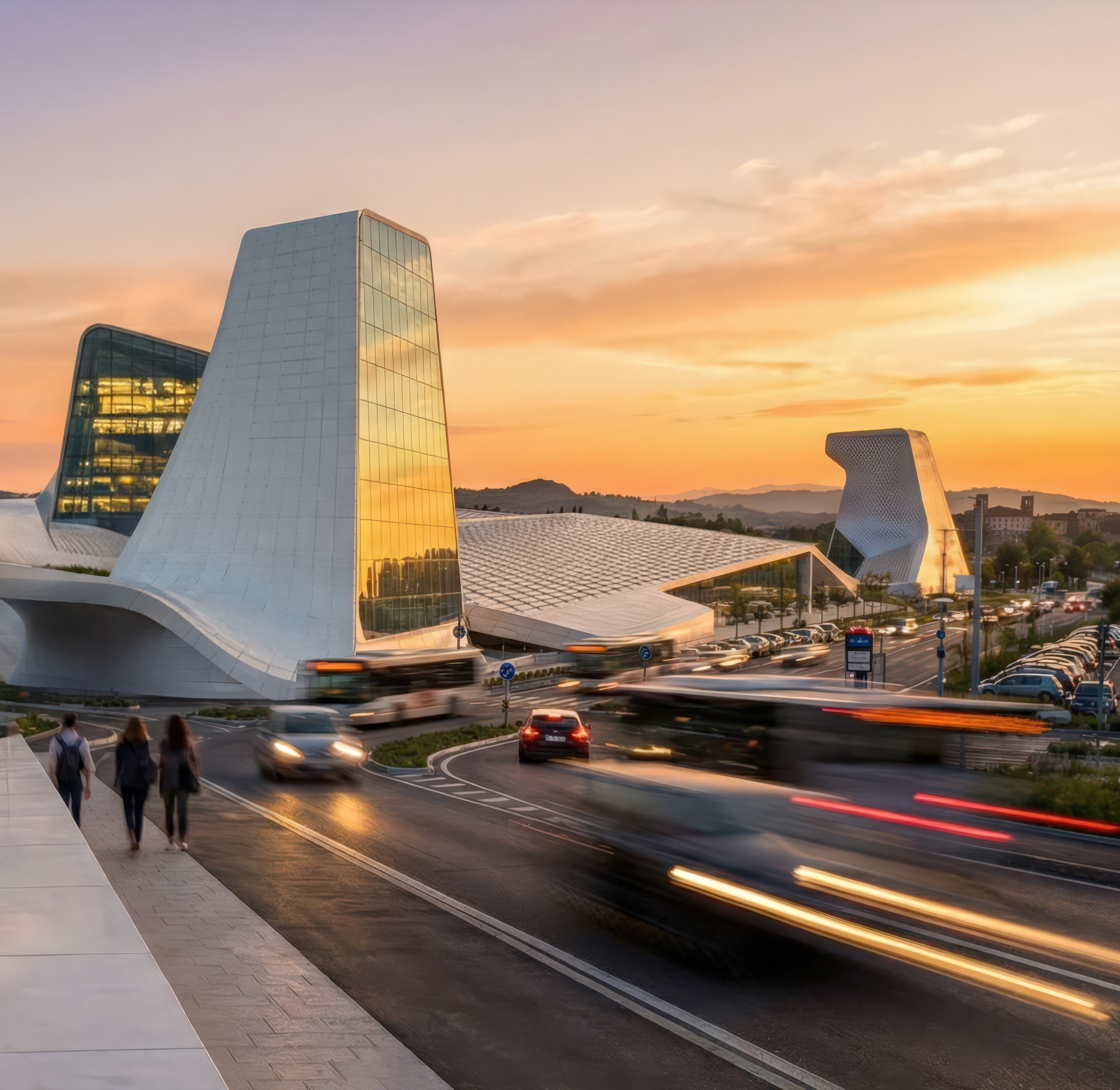 Street-level sunset view showing the sculpted white volumes and glass towers rising above the roadway with motion-blurred traffic