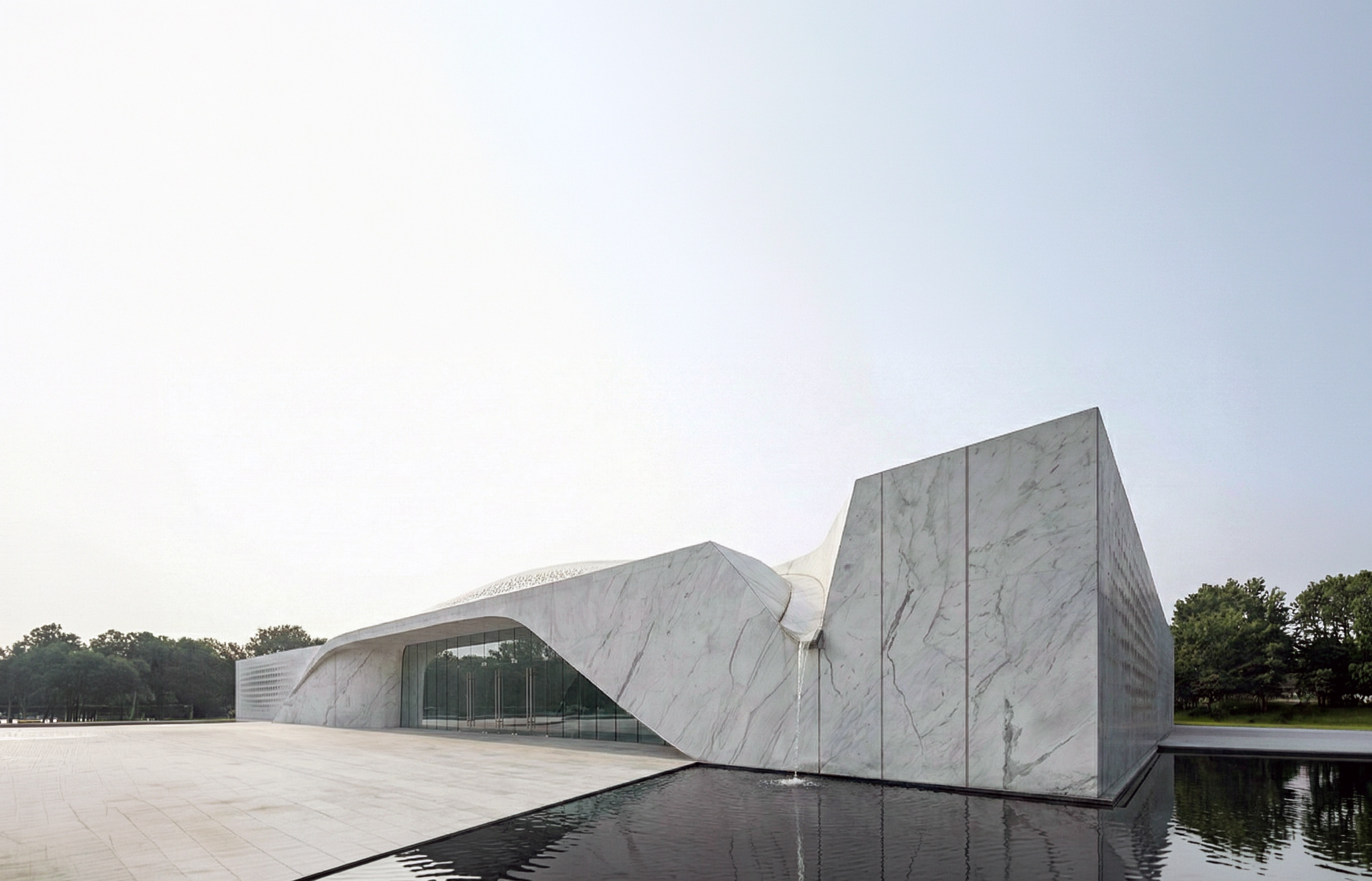 Beukenhof Crematorium exterior with folded marble facade, reflecting pool, and landscape setting