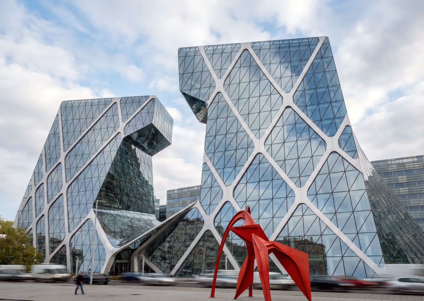 Budapest Bank Tower with its distinctive diamond-patterned glass facade and red sculpture at street level under cloudy skies