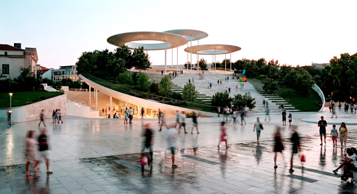 Approach view of the Burgas Performing Arts Center with sweeping terraced steps, disc-shaped canopy structures, and a lively public plaza