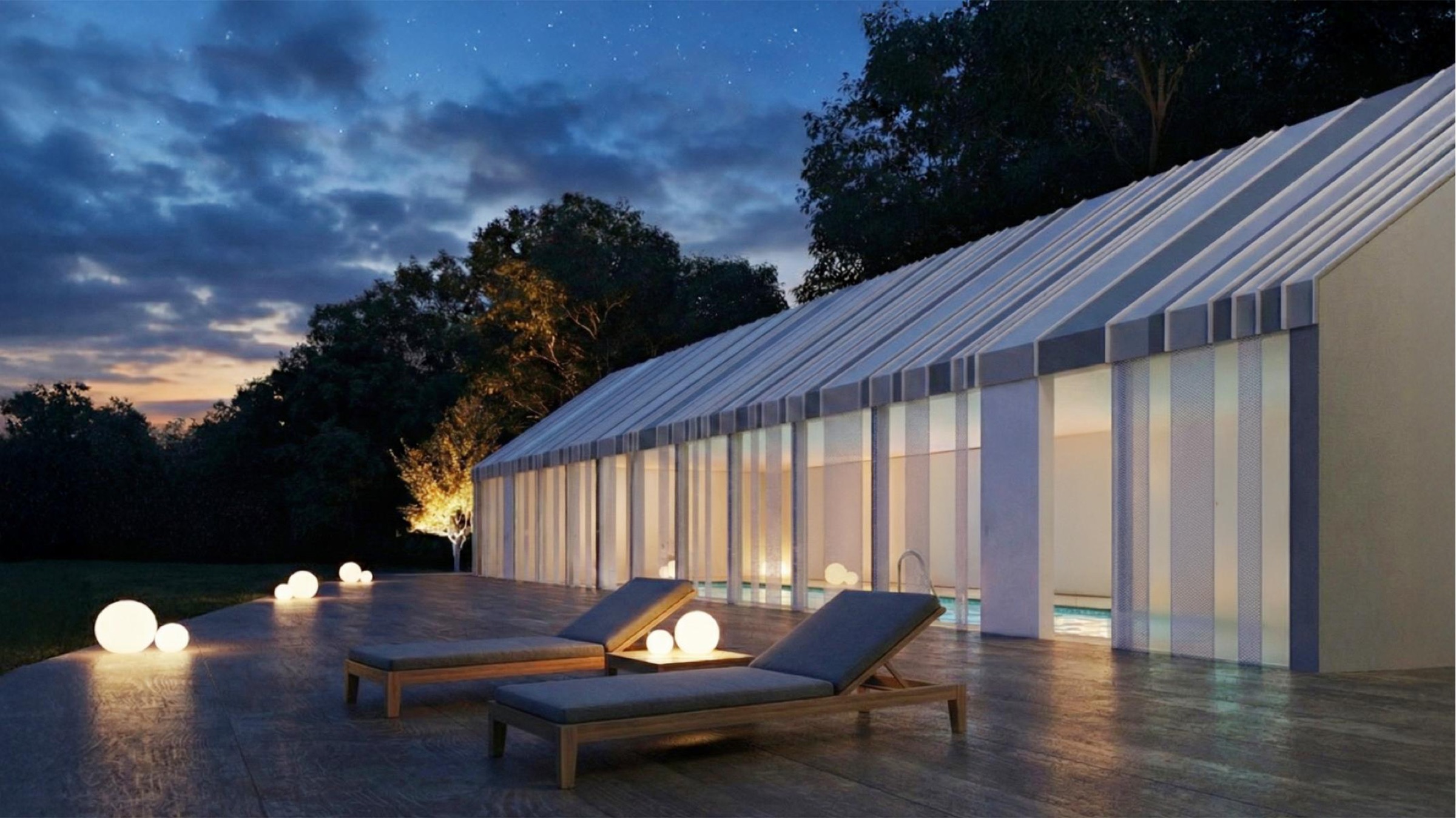 Exterior evening view of the pavilion from the terrace — pitched roof form with glazed walls glowing from within, lounge chairs and spherical lights on the timber deck, trees silhouetted against the dusk sky