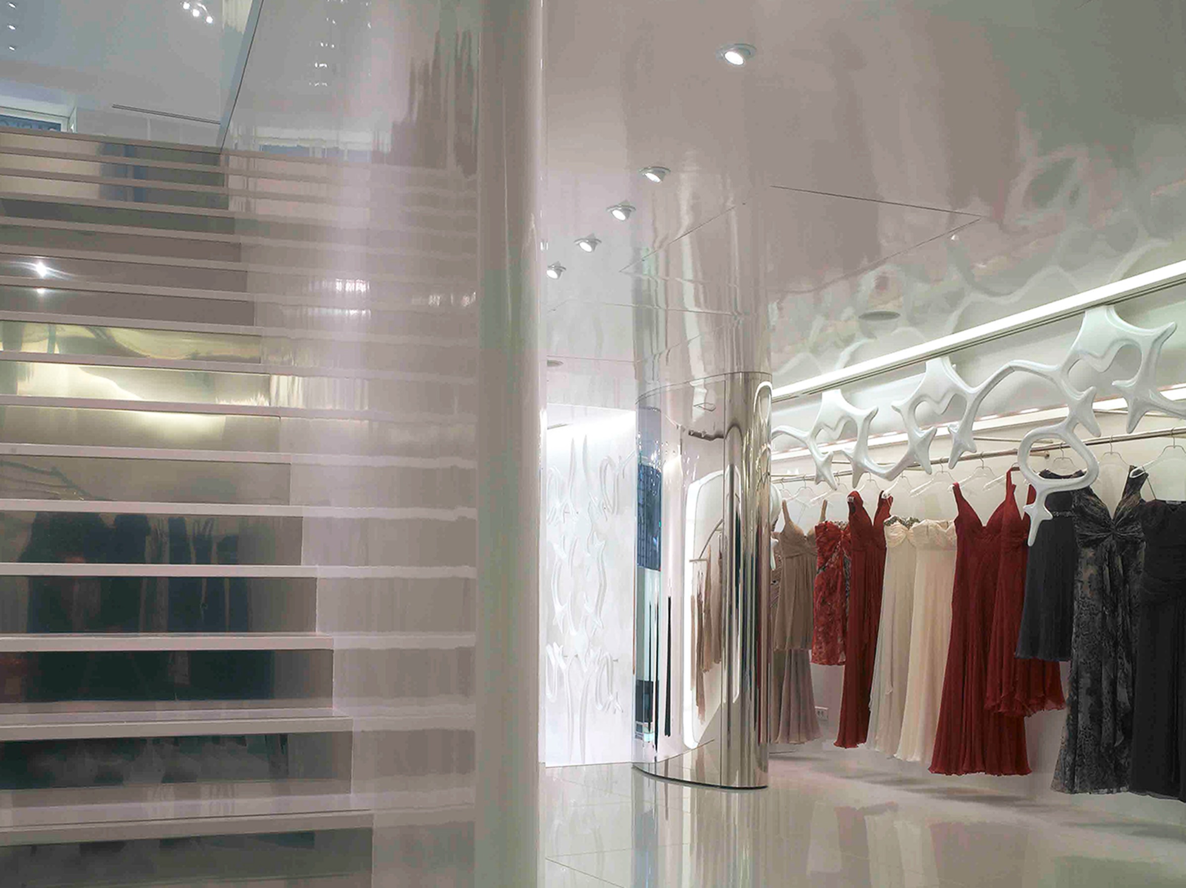 Glass staircase and mirrored cylindrical column with red and cream garments displayed along the fiberglass sculptural wall