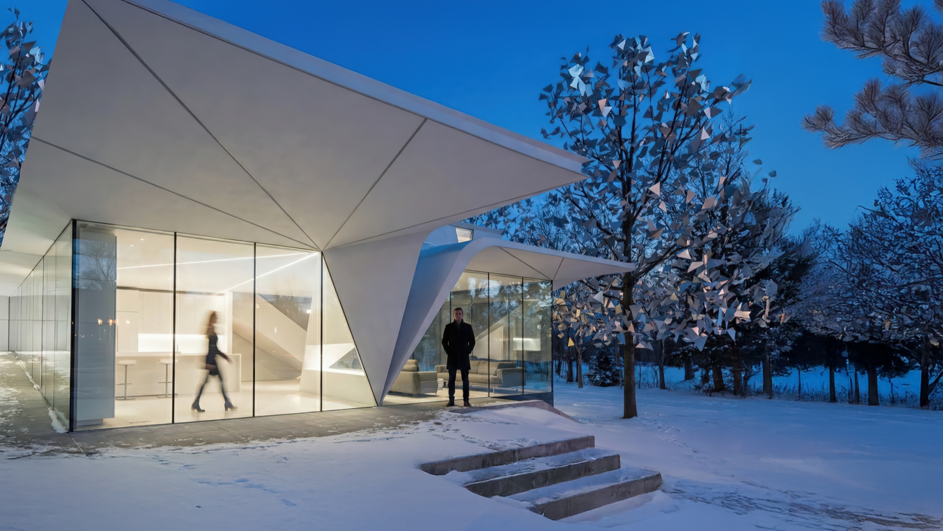 Evening view of the Cervelo House showing the angular canopy and illuminated glass facades framed by snow-covered trees