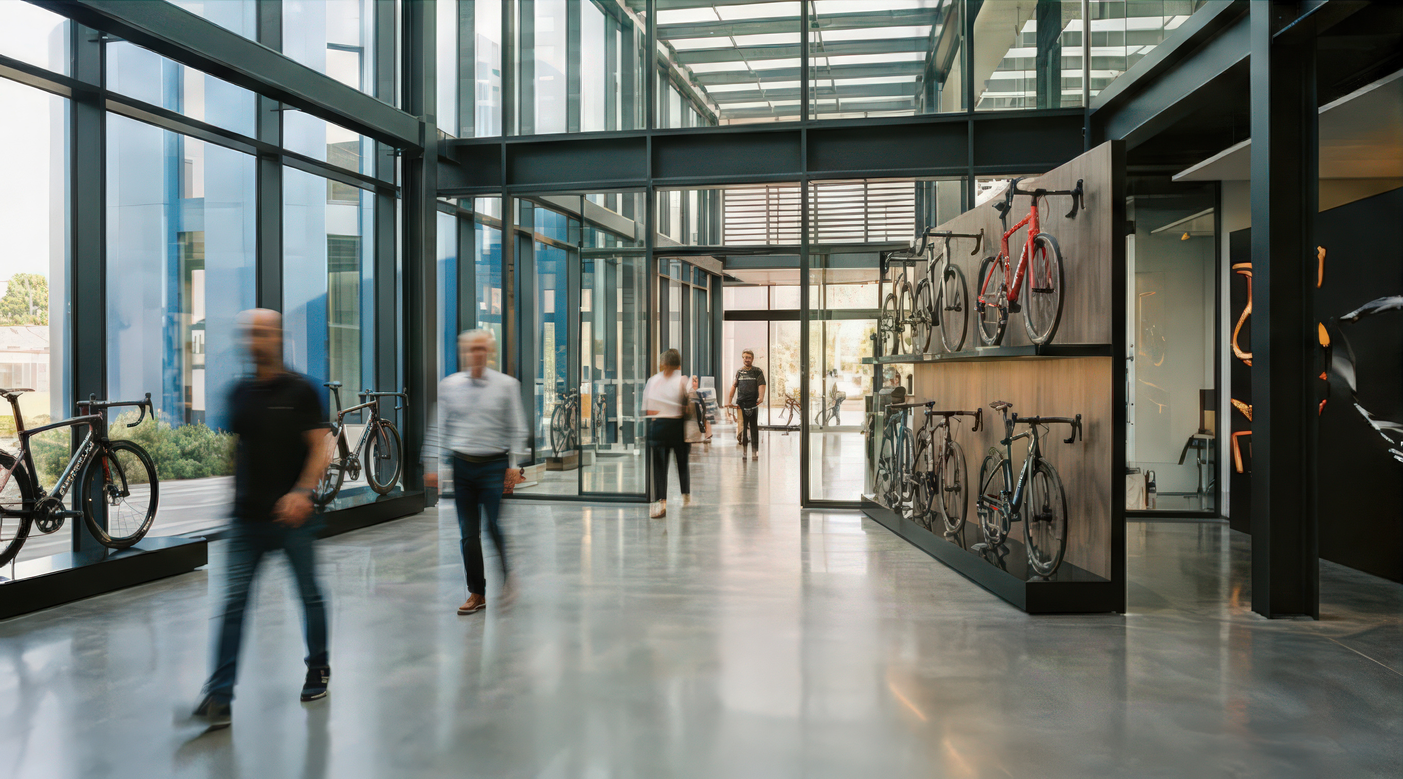 Interior of the annex with Pinarello bicycles displayed in glass-walled cabinets, motion-blurred figures walking through the corridor