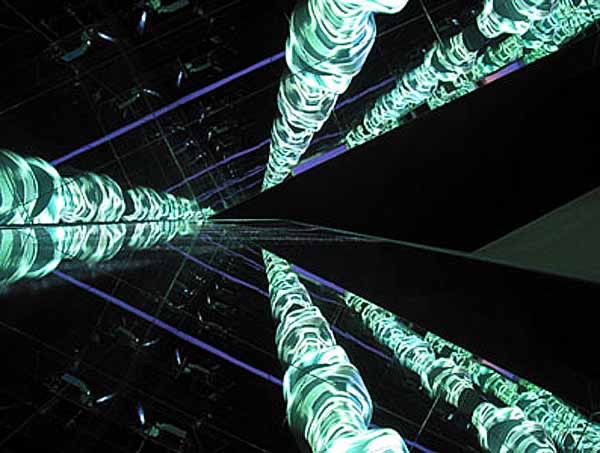 Abstract view looking up through the illuminated biomorphic spines of Fluxspace 3.0 — projected cityscapes wrapping the suspended armatures against the darkened ceiling