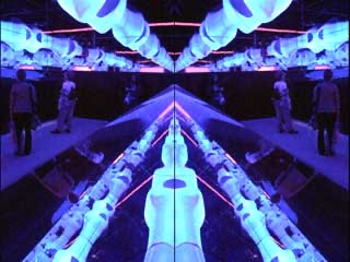 Visitors inside Fluxspace 3.0 surrounded by mirrored reflections and vivid blue-purple projected light across the biomorphic armatures