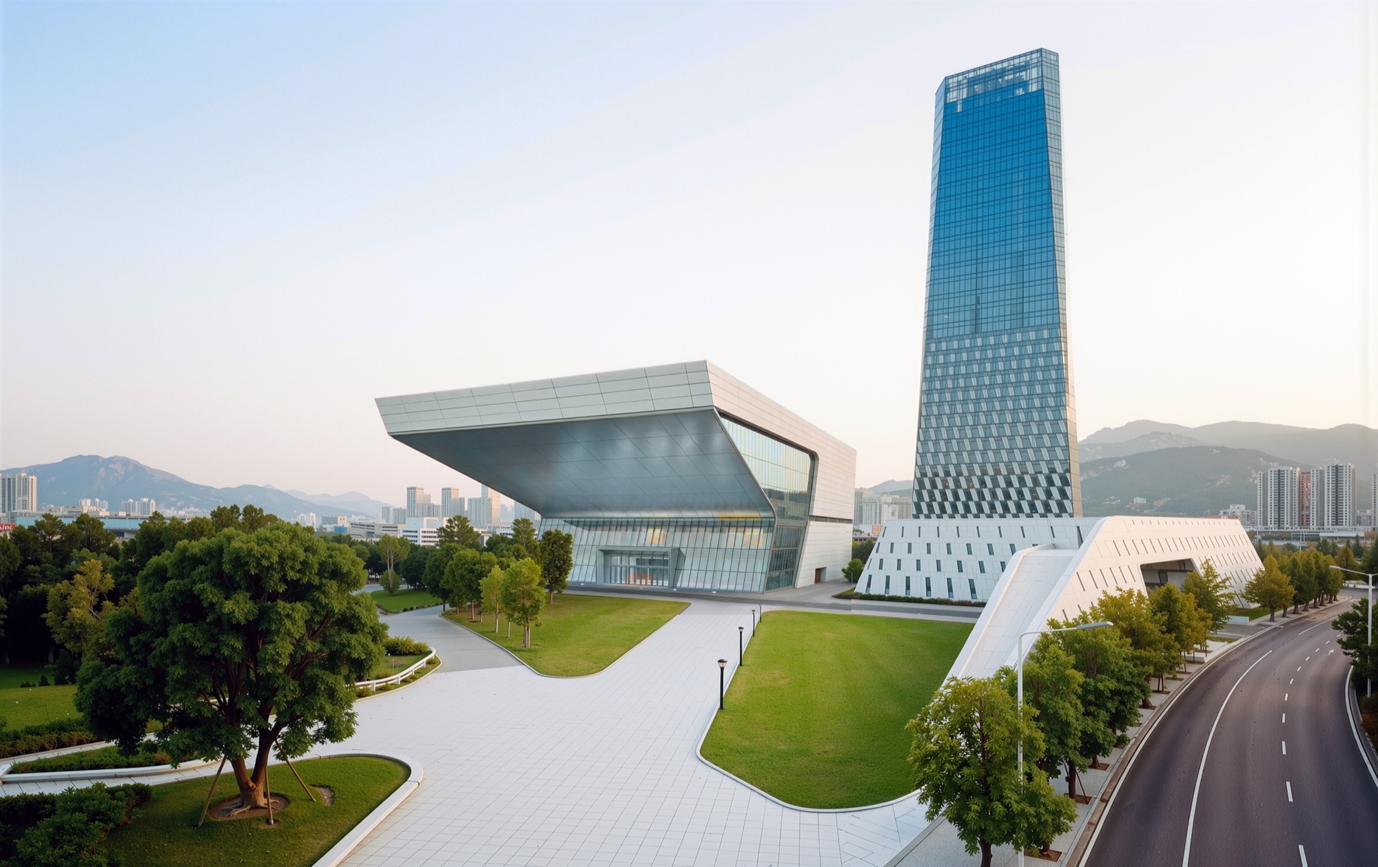 Elevated view showing the cantilevered performing arts hall, landscaped lawns, and the tower's faceted glass facade with mountains in the distance