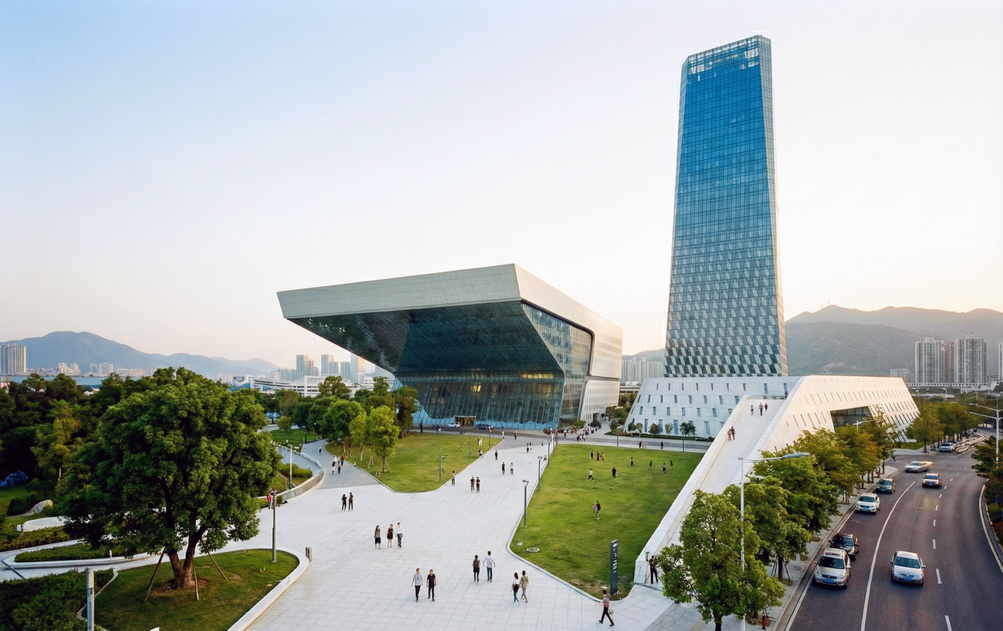 Overview of the campus from the southeast showing the performing arts center's dramatic cantilever, public plaza with pedestrians, the tower, and tree-lined pathways