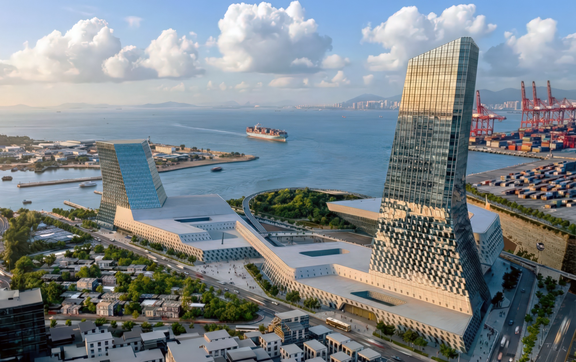 Aerial panorama of the Emerald Island campus from the harbor side, showing the twin towers flanking the performing arts center with container ships and port cranes beyond