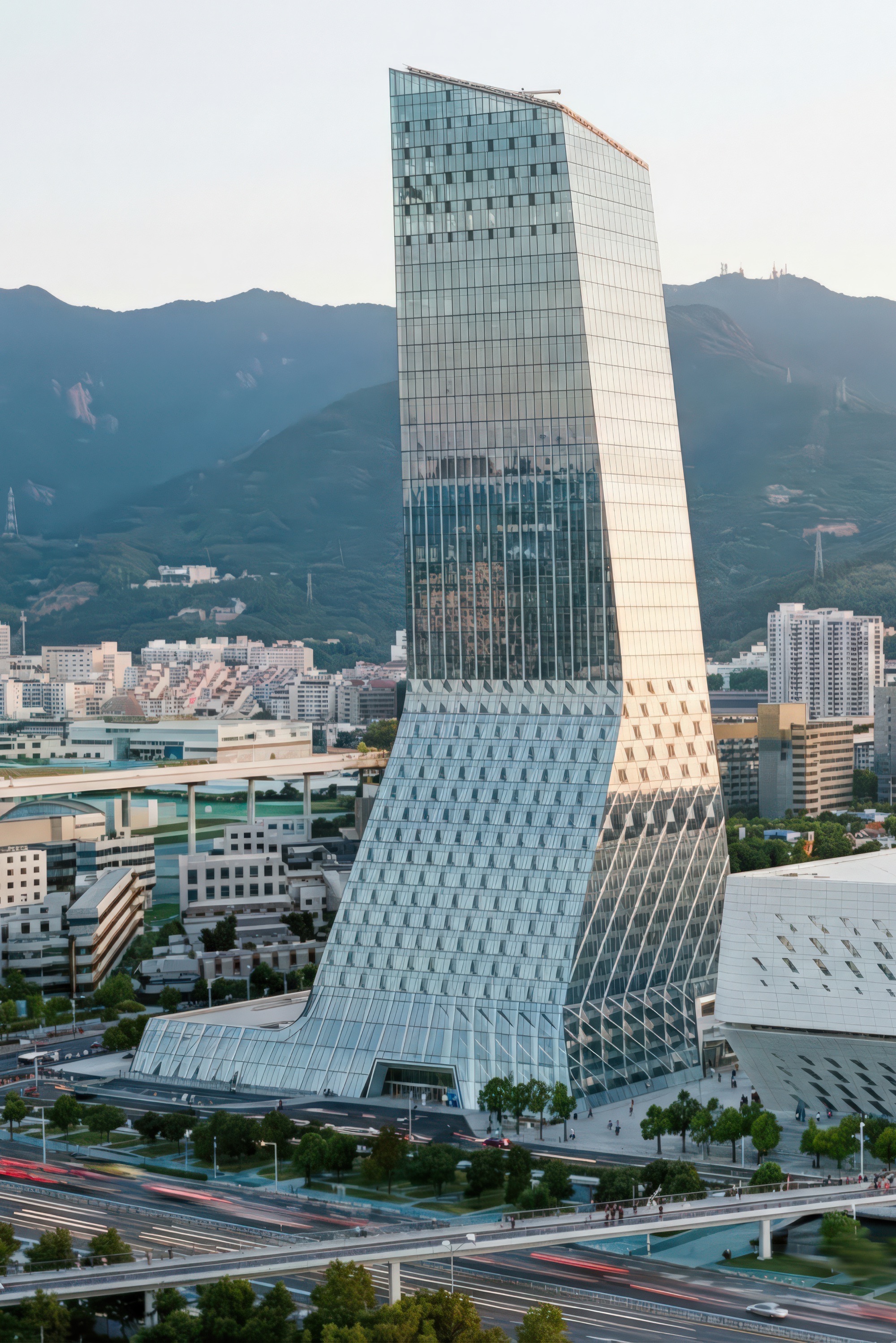 Portrait view of the twisting glass tower with diamond-patterned base podium and mountains in the background