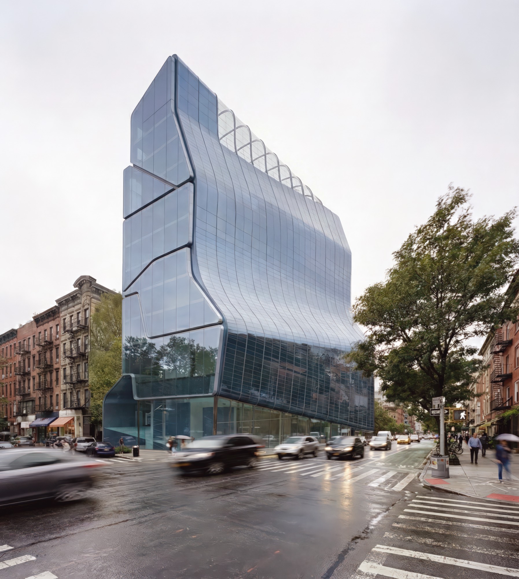 Full street-level view of the Eyebeam Center tower, a faceted glass-clad volume rising above a Chelsea intersection in New York City