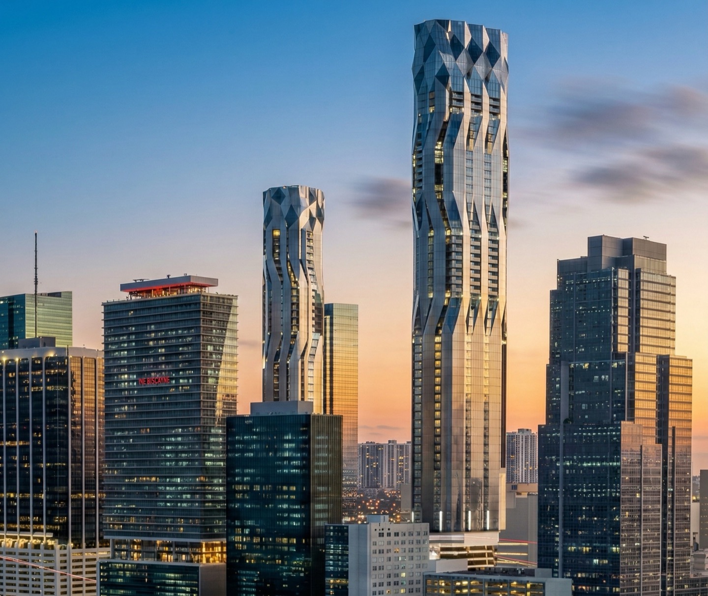 Close-up view of the twin Flagler Towers at golden hour showing the sculptural flowing facade and faceted glass crown elements against a warm sunset sky