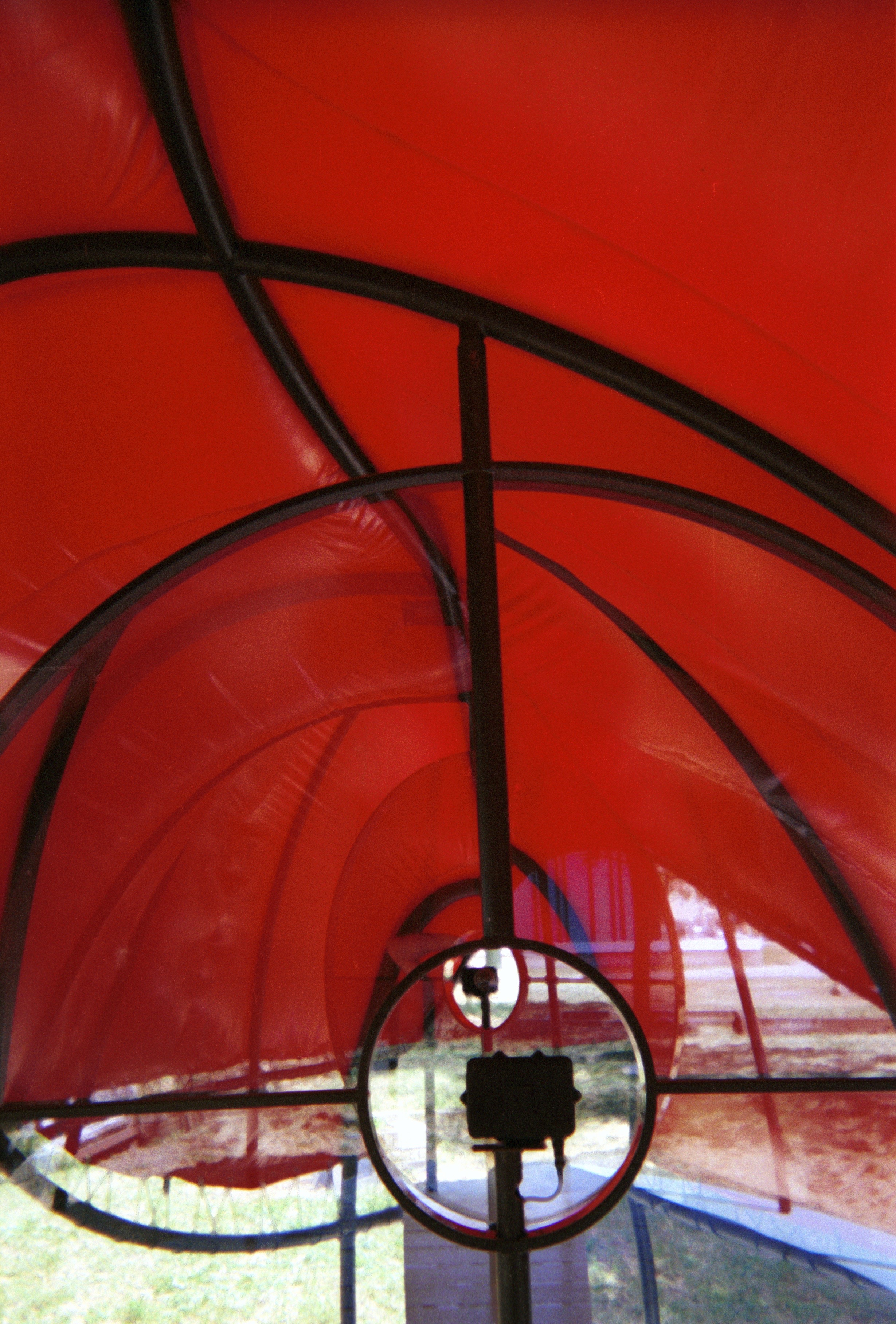 Abstract detail of the Flux Pavilion canopy — red pneumatic curves and black steel armatures against sky