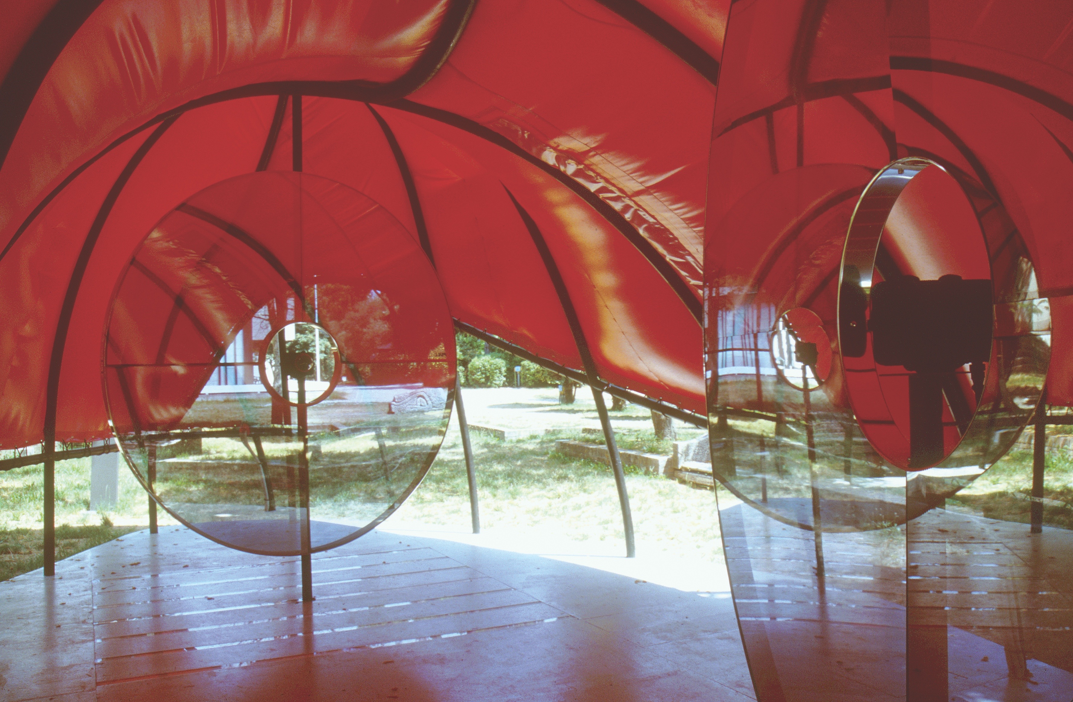 Interior view through the circular glass portals of the Flux Pavilion — red inflatable surfaces and steel framework visible