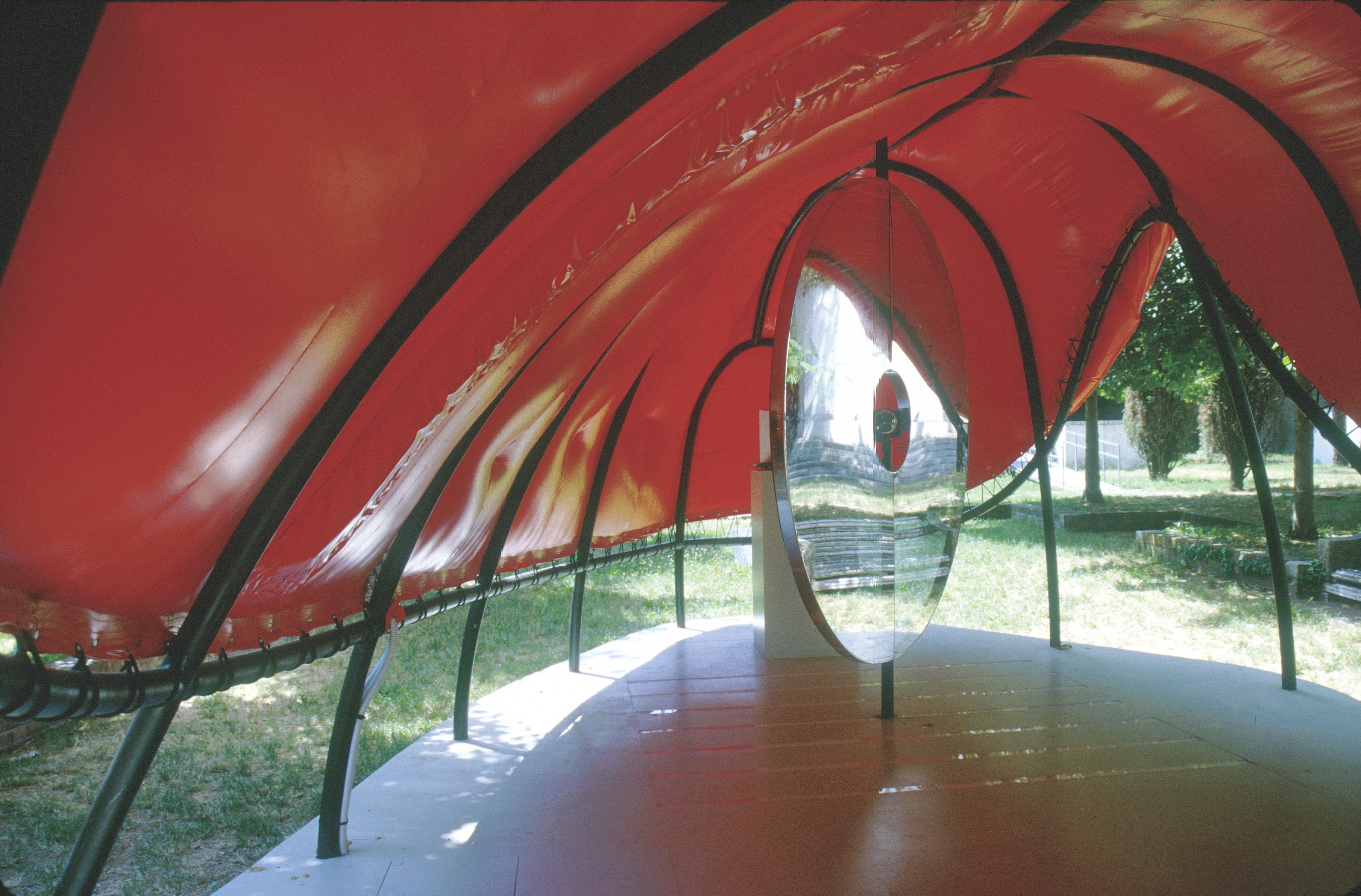 Interior of the Flux Pavilion — visitors walk through a red-canopied tunnel with circular glass portals framing views of the Giardini