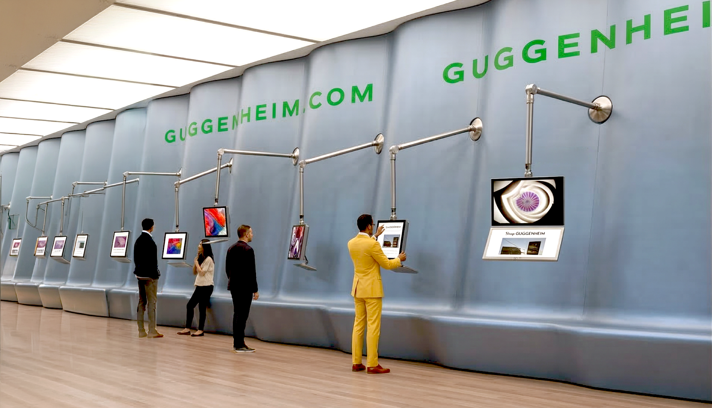Visitors browsing articulated arm-mounted screens along a curved metallic wall branded GUGGENHEIM.COM, displaying artworks and virtual museum content