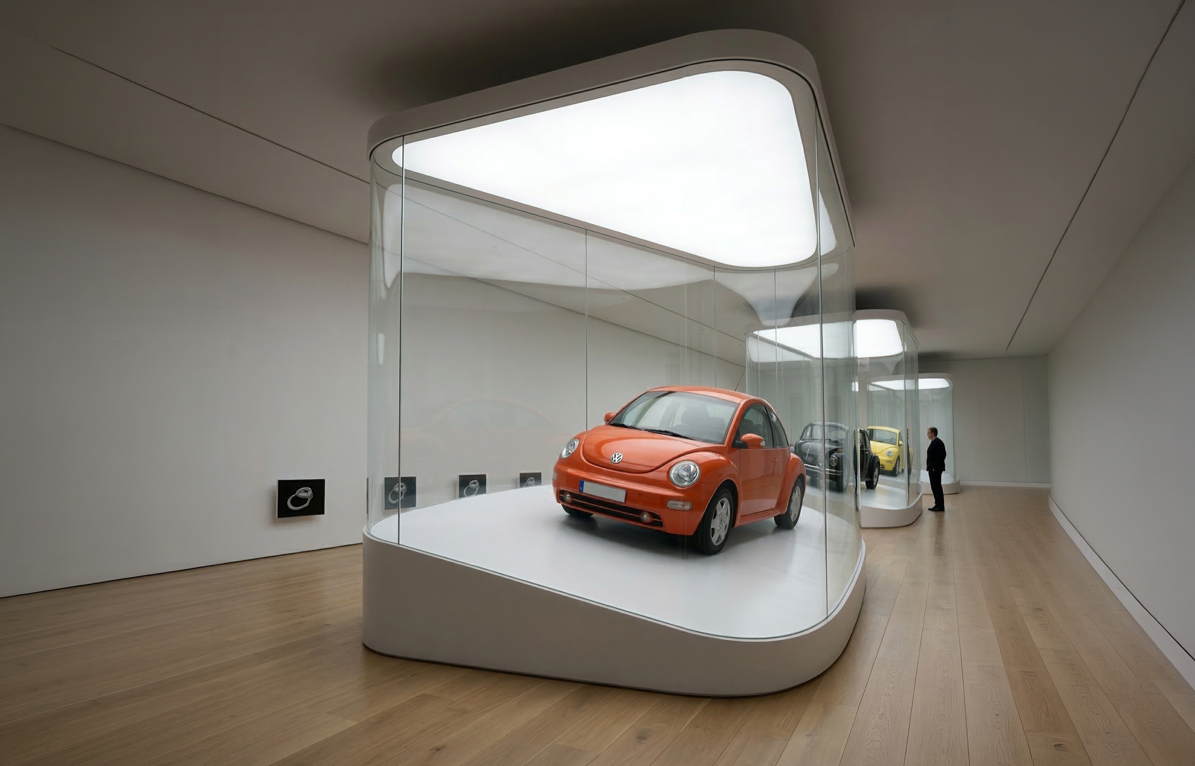 Large curved glass vitrine with luminous ceiling enclosing a curated design object, smaller gallery monitors mounted along the adjacent wall