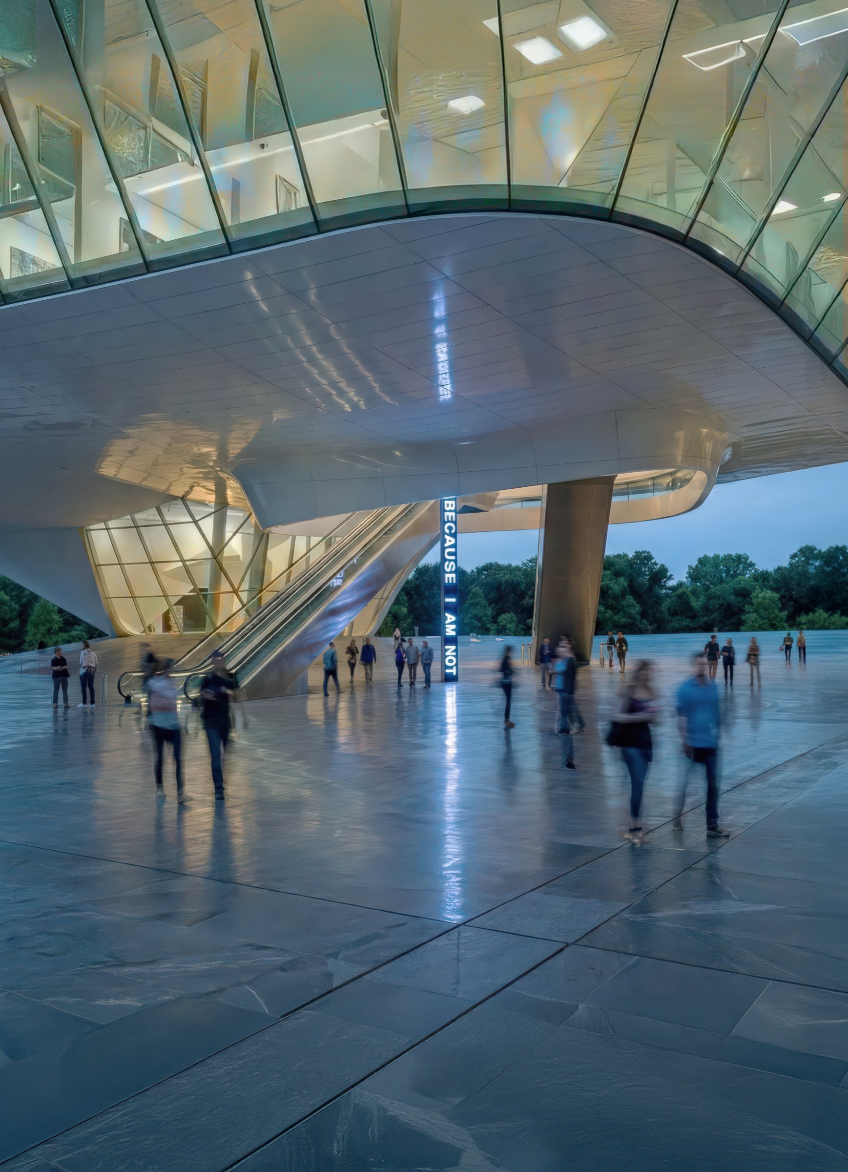 Vertical view of the inclined escalator volume rising from the Zócalo plaza into the museum above, with visitors on the escalator and the canyon landscape visible beyond angled glazing at dusk