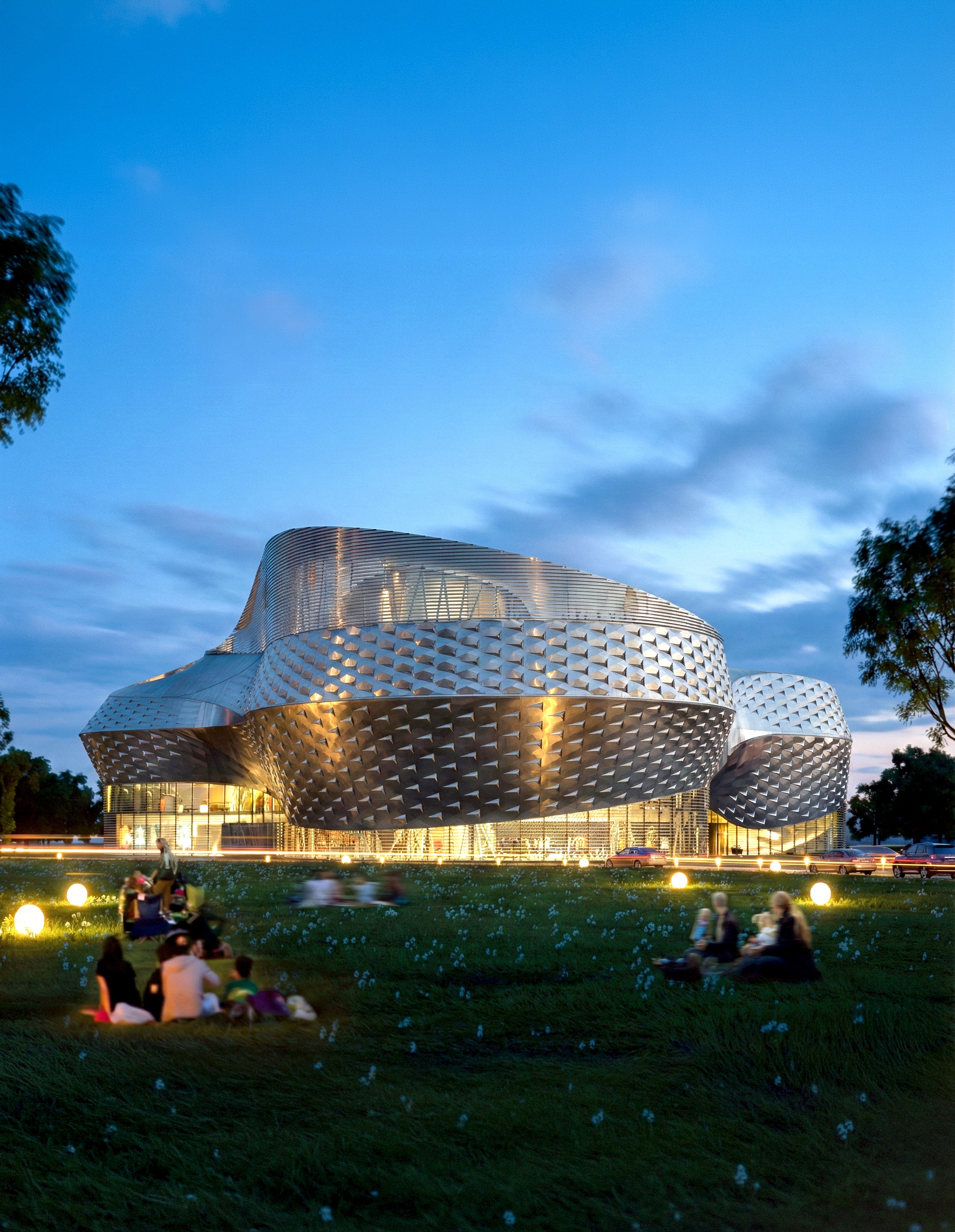 Exterior dusk view of the House for Hungarian Music with its sculptural metallic facade glowing warmly against a twilight sky
