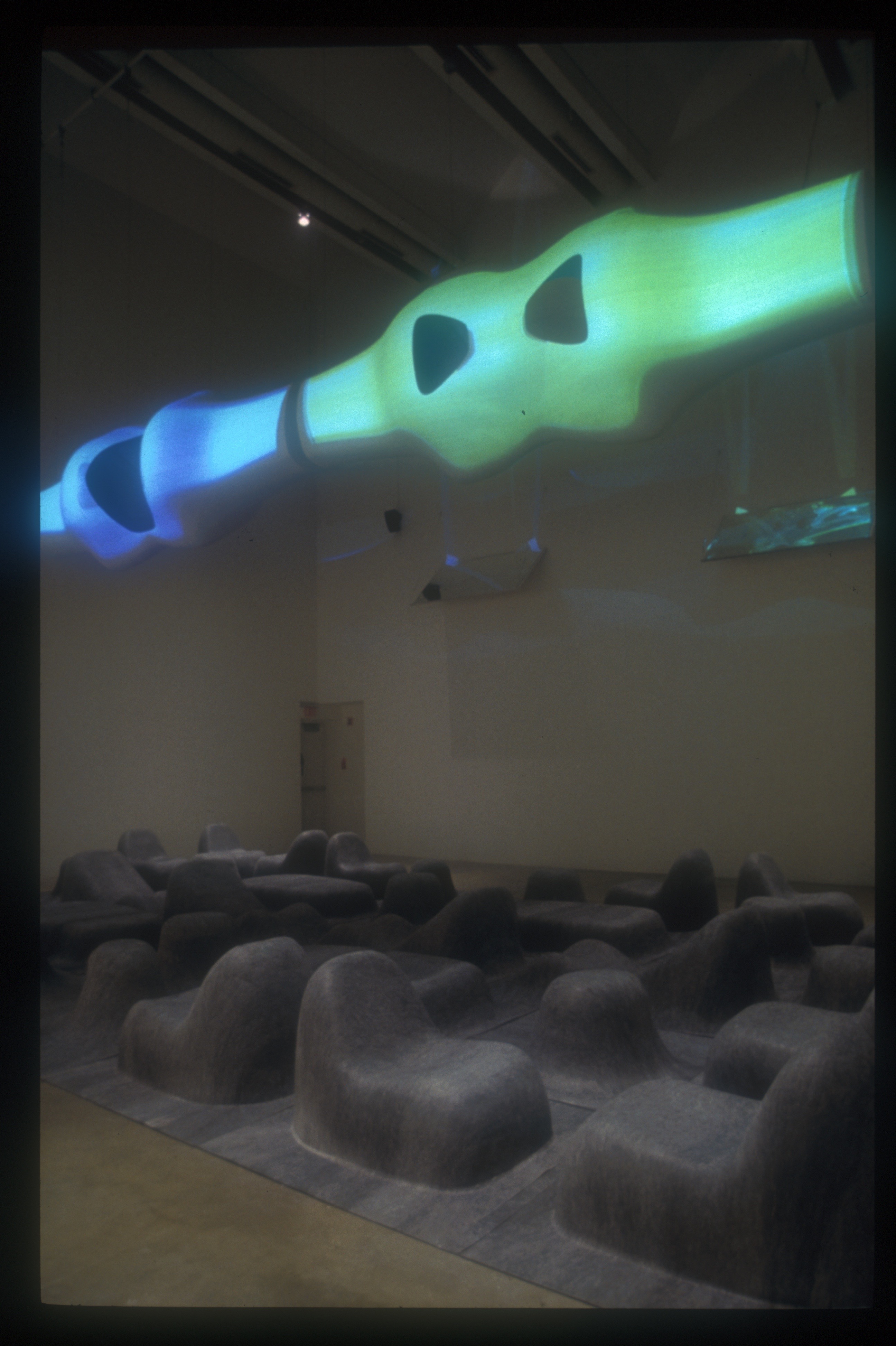 Detail of the sculptural felt seating landscape with a suspended biomorphic form glowing green and blue in the background