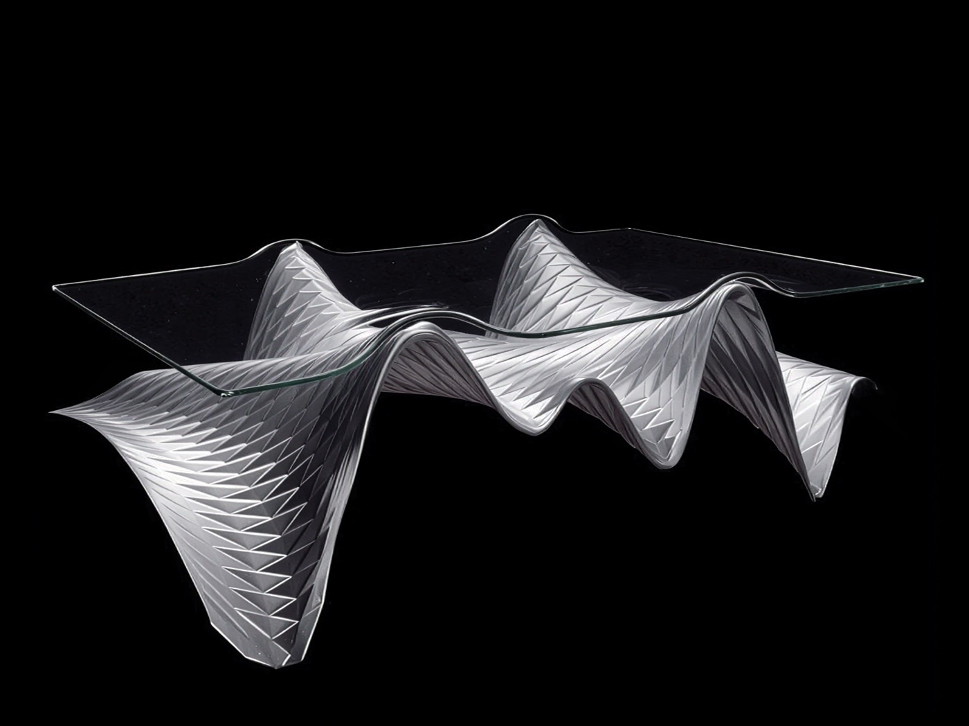 Three-quarter view of the Ivo_03 table showing the undulating Tula steel base with slumped glass top against a black background