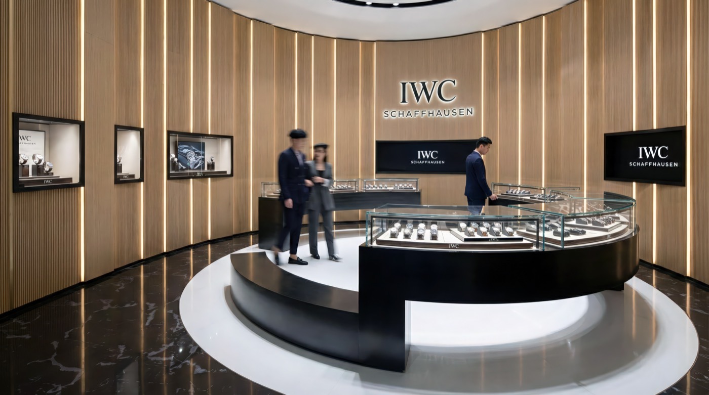 Central display island with curved glass vitrine showcasing IWC watches, surrounded by vertical golden wall panels