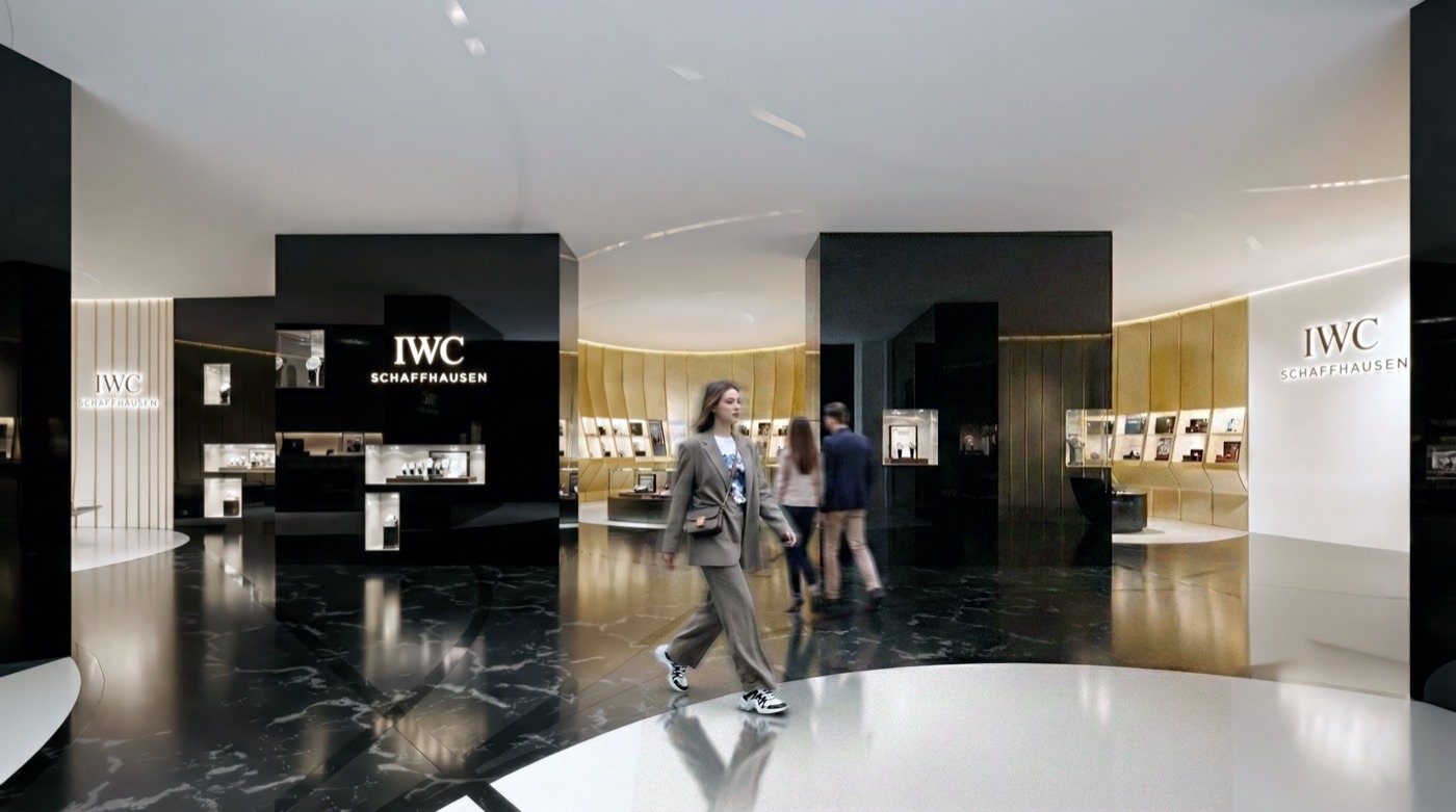 Wide view of the IWC boutique interior with black display volumes, golden wall panels, and visitors browsing