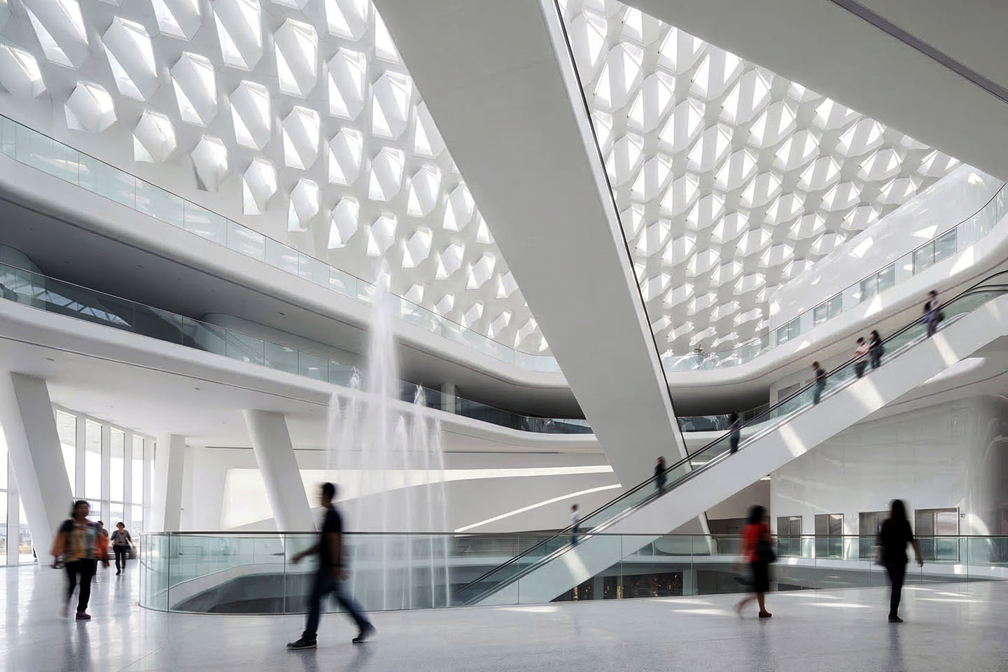 Interior of the central atrium with diamond-patterned skylight flooding the space with light, fountain, escalators, and visitors in motion