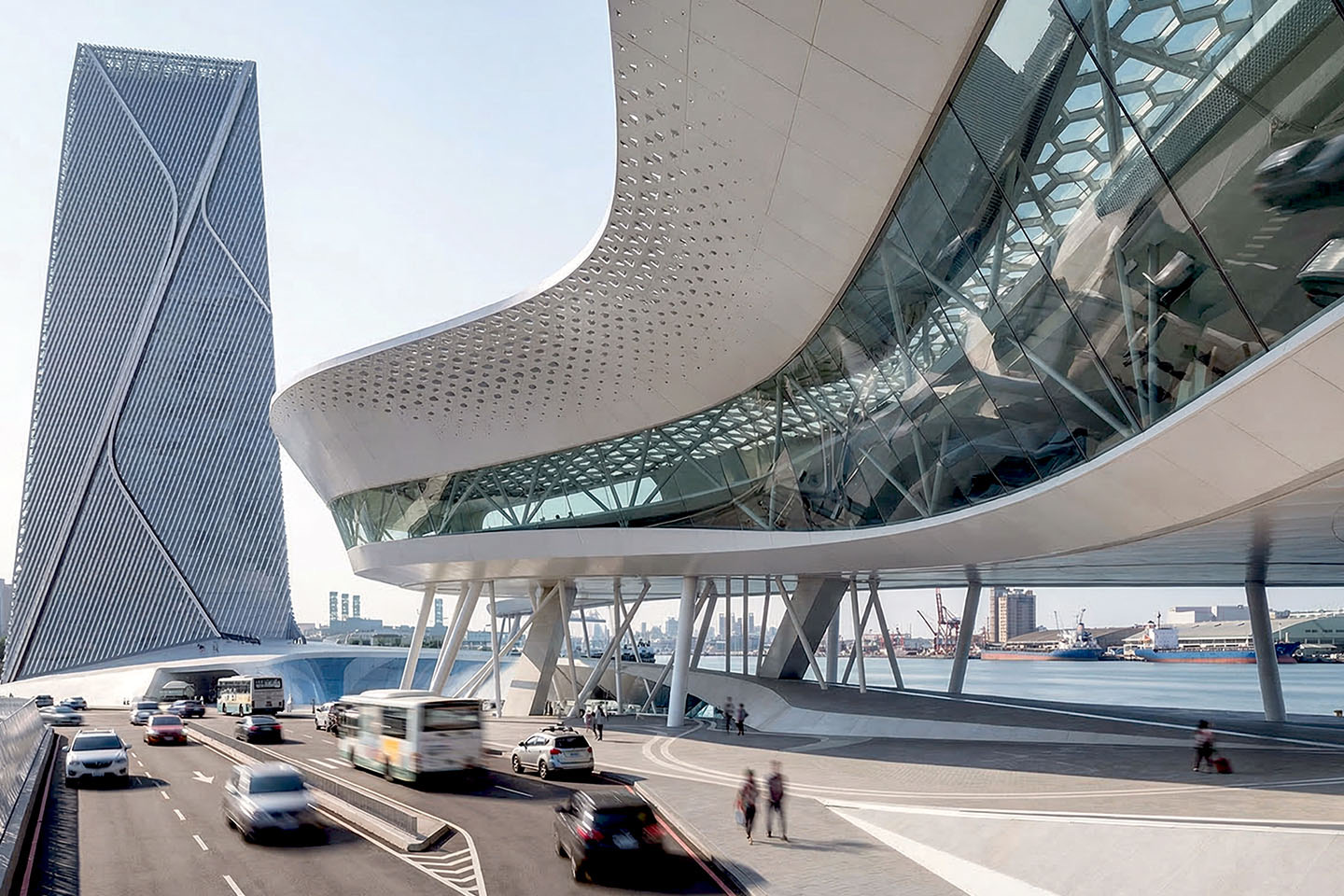 Exterior view of the perforated canopy and tower with cross-braced facade, roadway passing beneath, harbor and port operations visible beyond