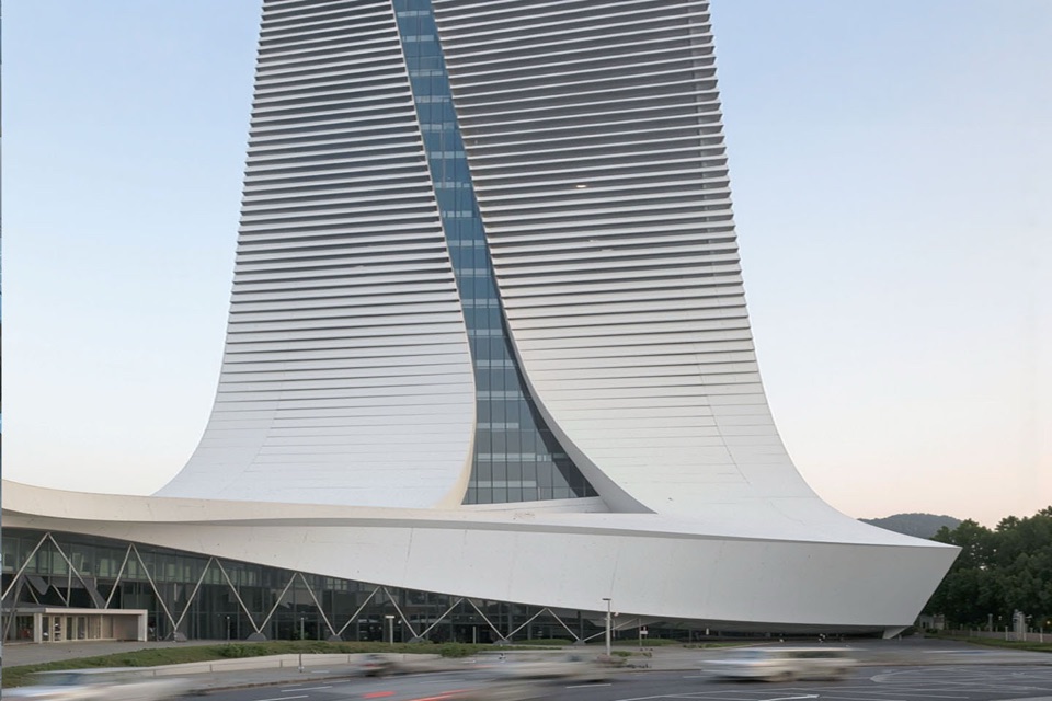 The 70-meter gateway tower with louvered facade and sweeping curved glass slot rising above the terminal canopy at dusk
