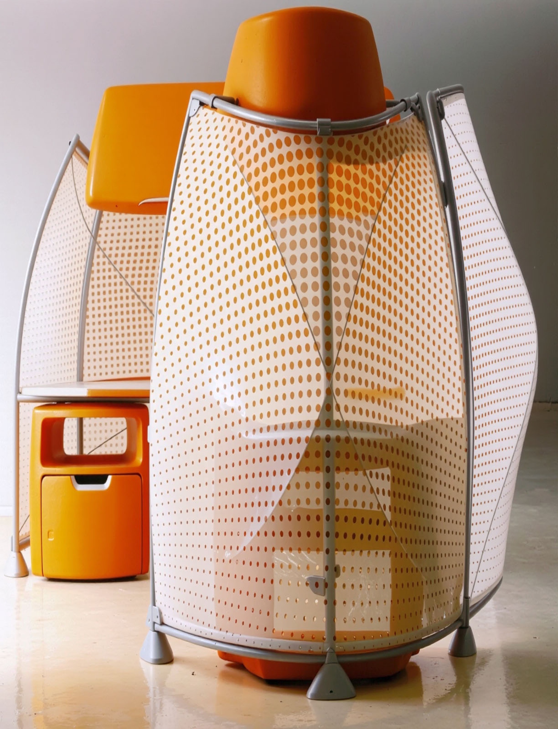 Close-up detail of an A3 workstation with orange perforated screens on elliptical steel frames, showing the overhead storage unit and mobile storage cart