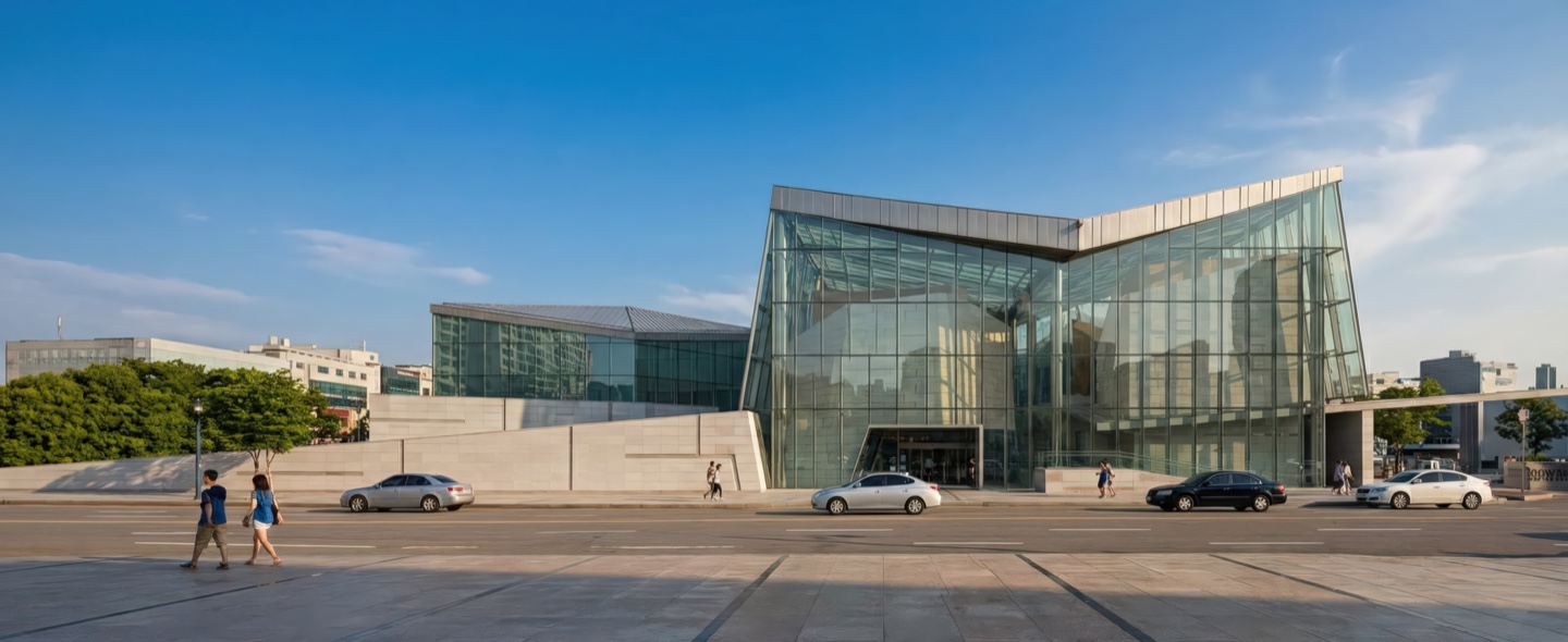Daytime exterior view of the museum complex under clear skies showing the faceted glass volumes rising above a stone plinth along the public plaza