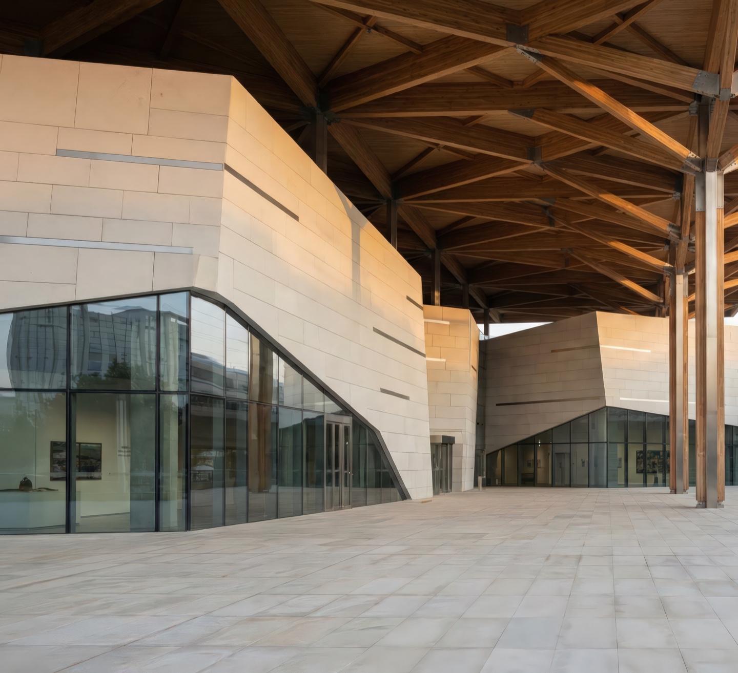Detail of the covered outdoor terrace with exposed timber truss canopy framing angular stone-clad gallery volumes and glazed curtain walls
