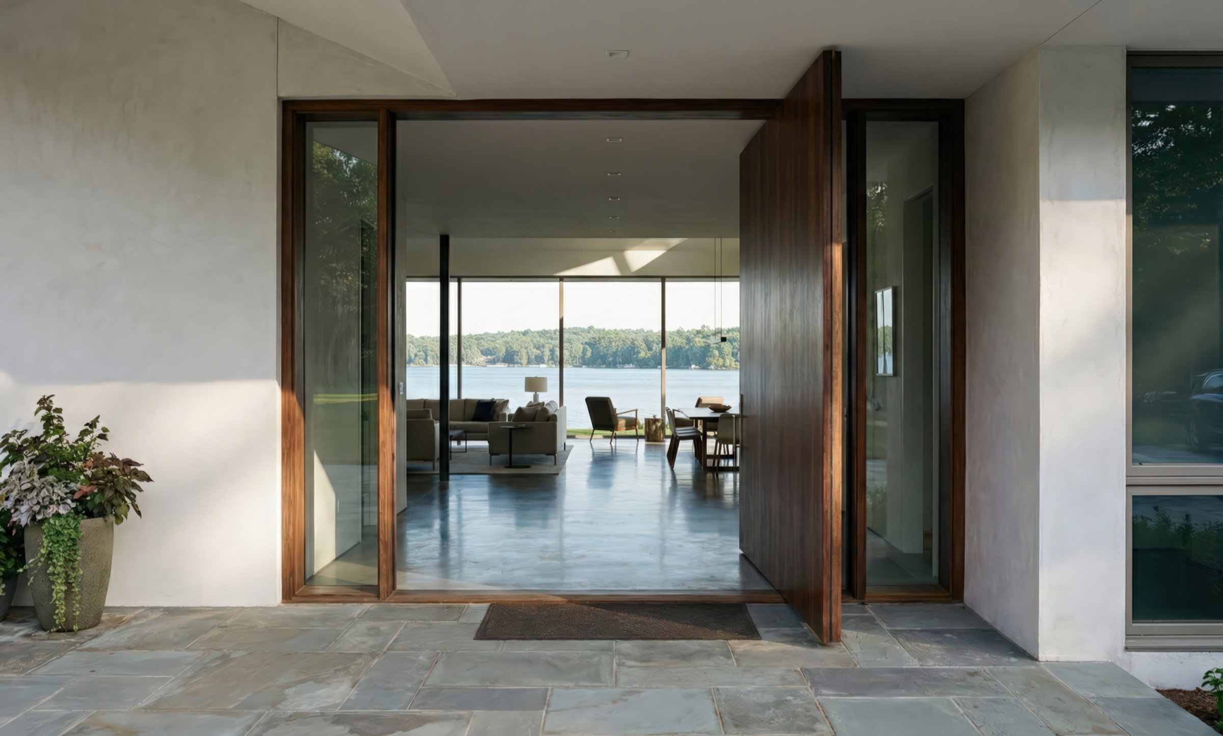 Walnut-framed pivot door entrance to Lakeview House revealing an open-plan interior with polished concrete floors and panoramic lake views beyond