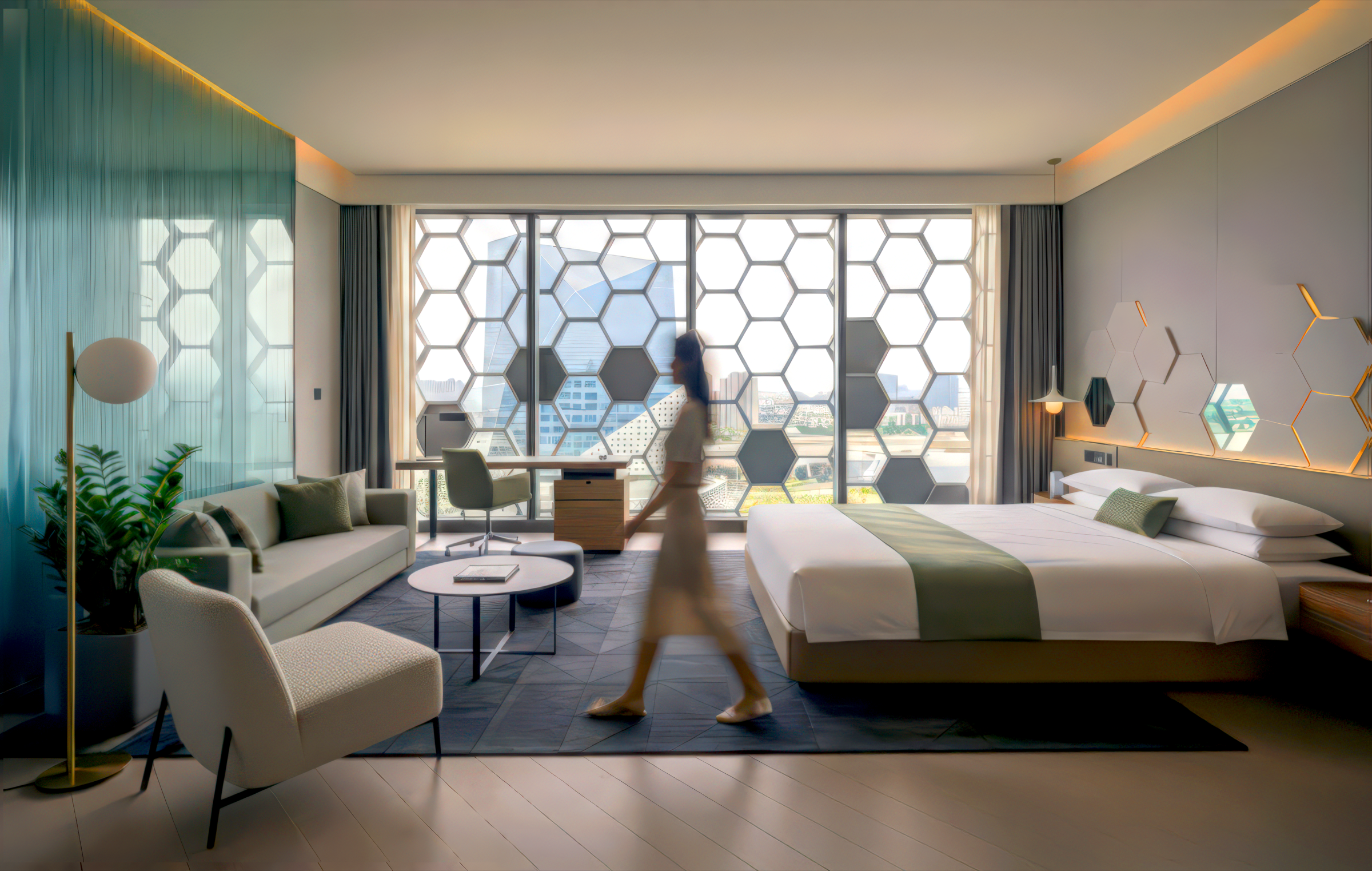 Deluxe guest room with hexagonal window wall filtering daylight, olive and white color palette, sofa seating area, work desk, and a guest walking through the space
