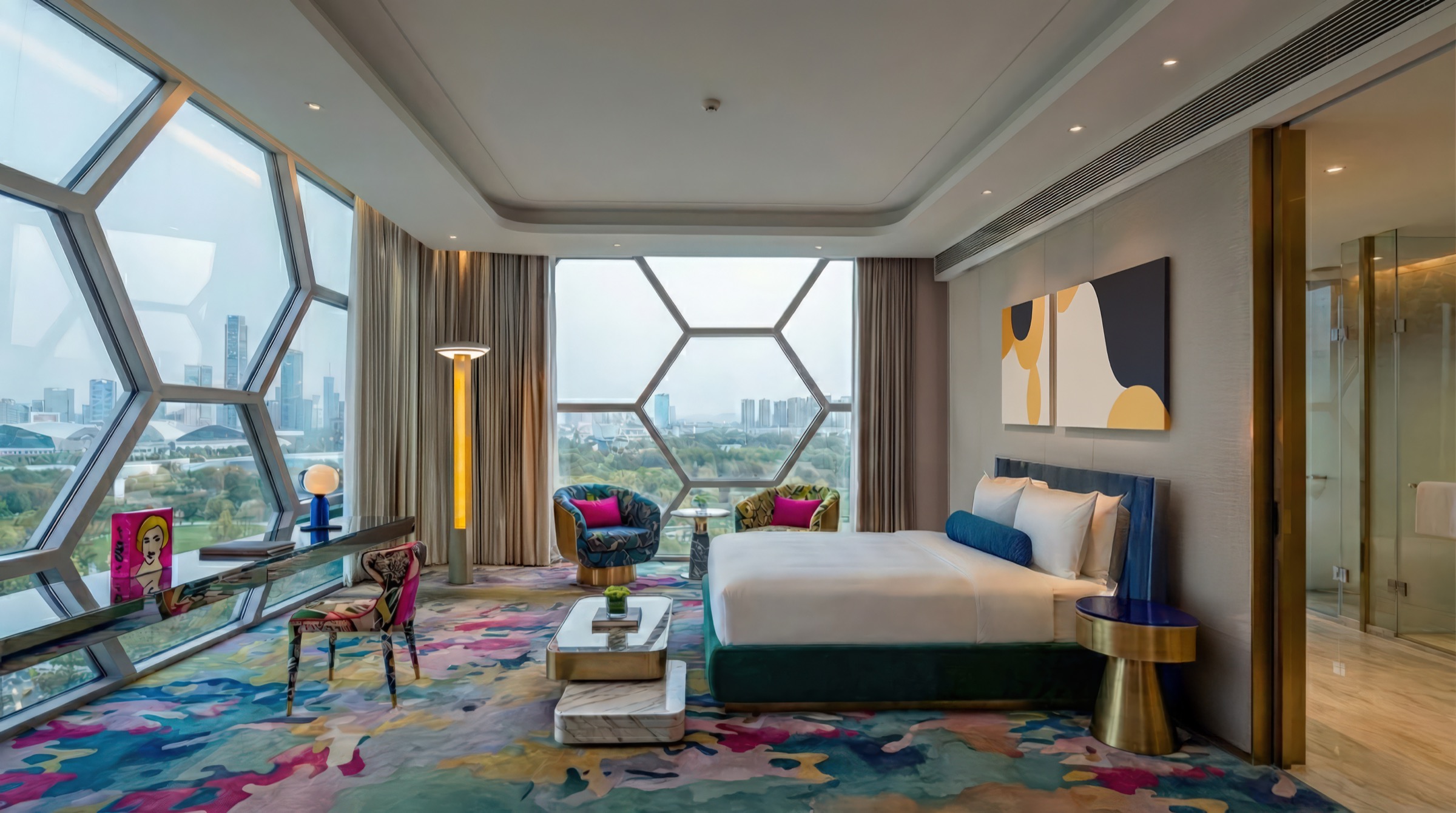 Vibrant guest suite with floor-to-ceiling hexagonal windows framing the Changsha cityscape, colorful abstract carpet, emerald velvet bed, pop-art furnishings, and contemporary artwork