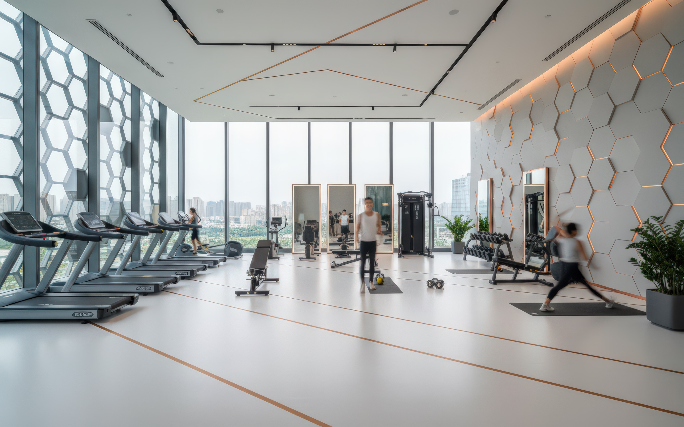 High-floor fitness center with hexagonal facade glazing, exercise equipment along the window wall, white hexagonal accent wall with amber LED outlines, and guests exercising