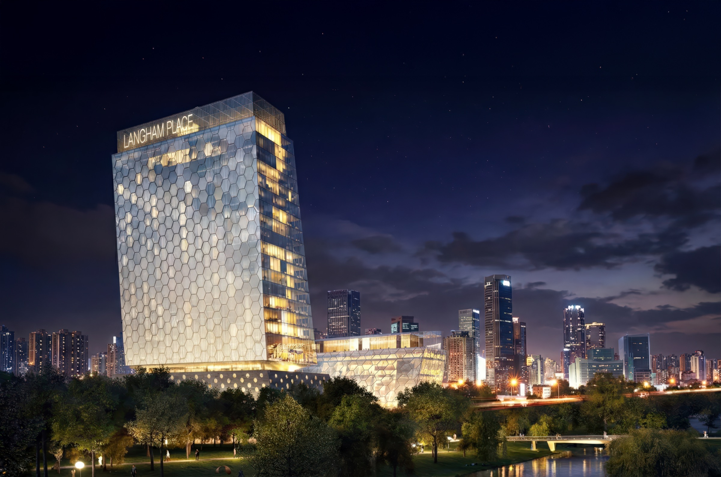 Langham Place Changsha tower illuminated at night with its hexagonal glass facade glowing warmly against the Changsha skyline and river